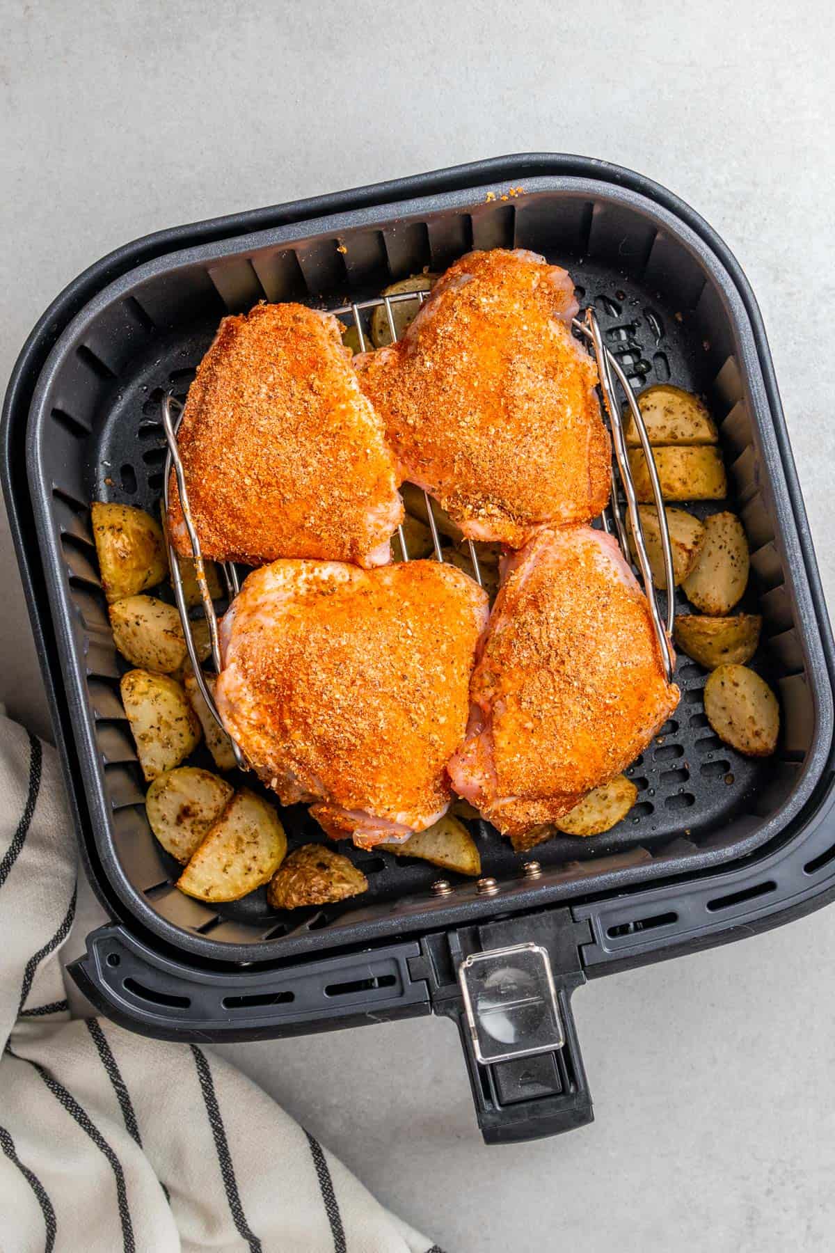 seasoned potatoes and chicken thighs in the air fryer basket 