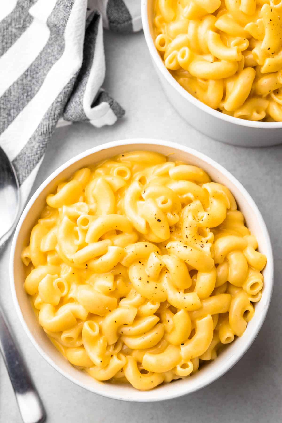 Mac and cheese in a white bowl with spoons and a cloth