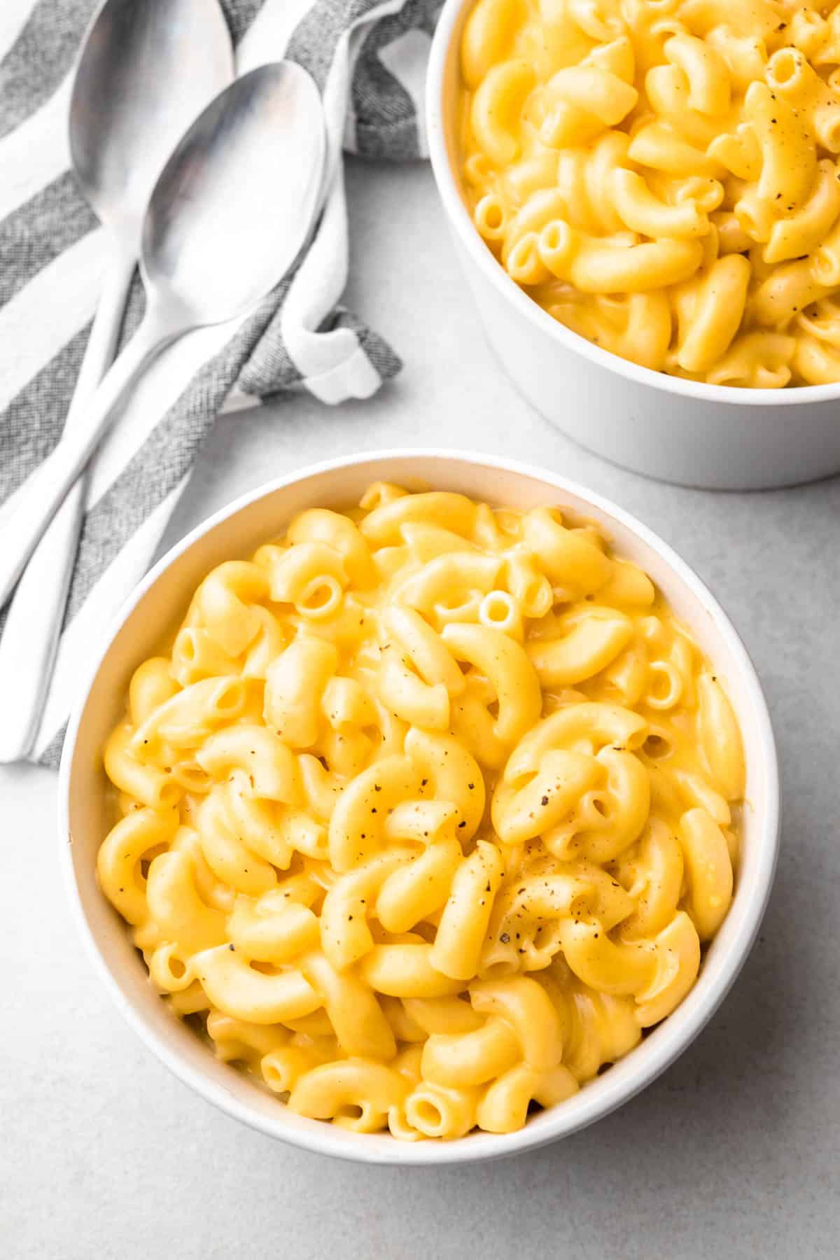 Mac and cheese in white bowls with spoons and a striped cloth