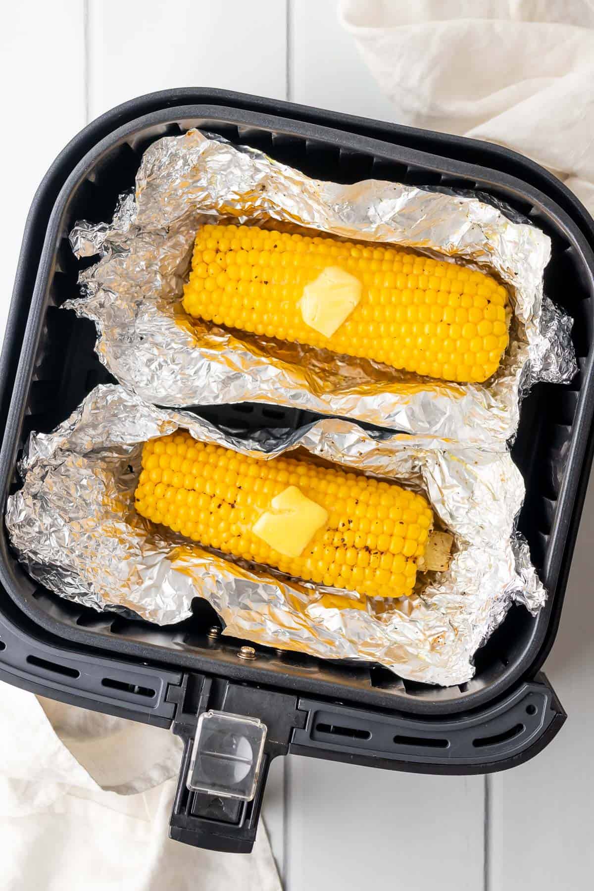 corn on the cob in foil in the air fryer basket with butter