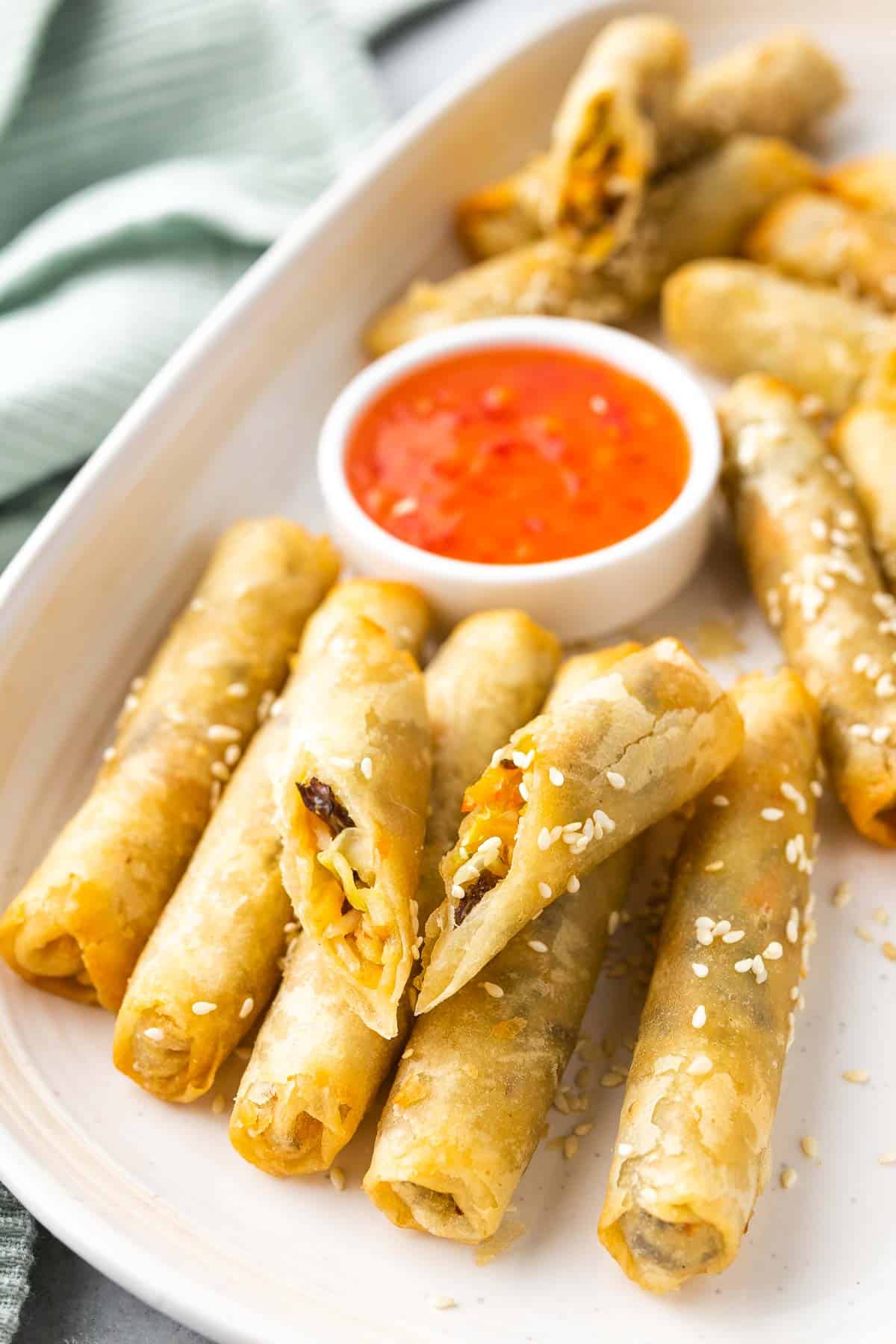 egg rolls served on a white platter with sweet chilli sauce and more sesame seeds
