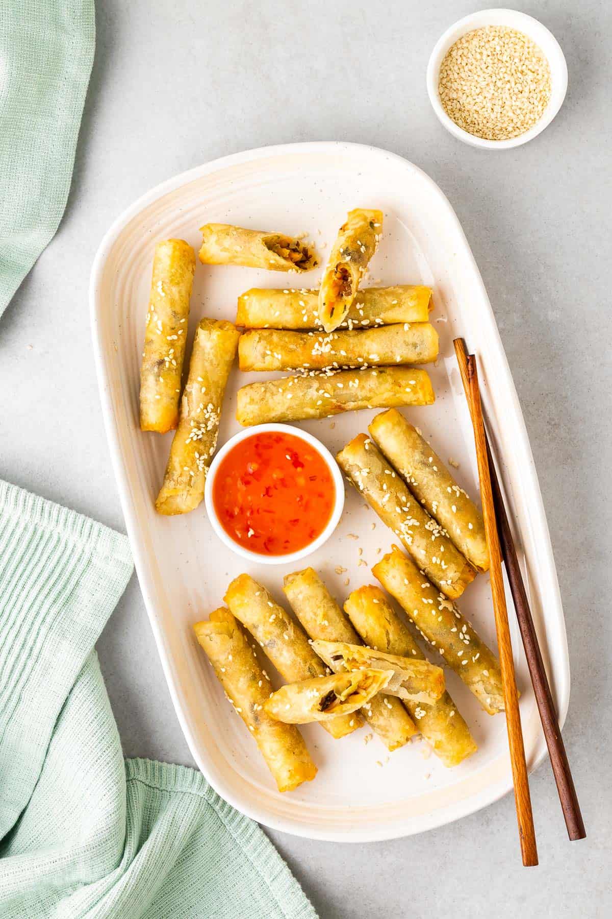 cooked air fryer egg rolls with sweet chili sauce and sesame seeds on a serving platter