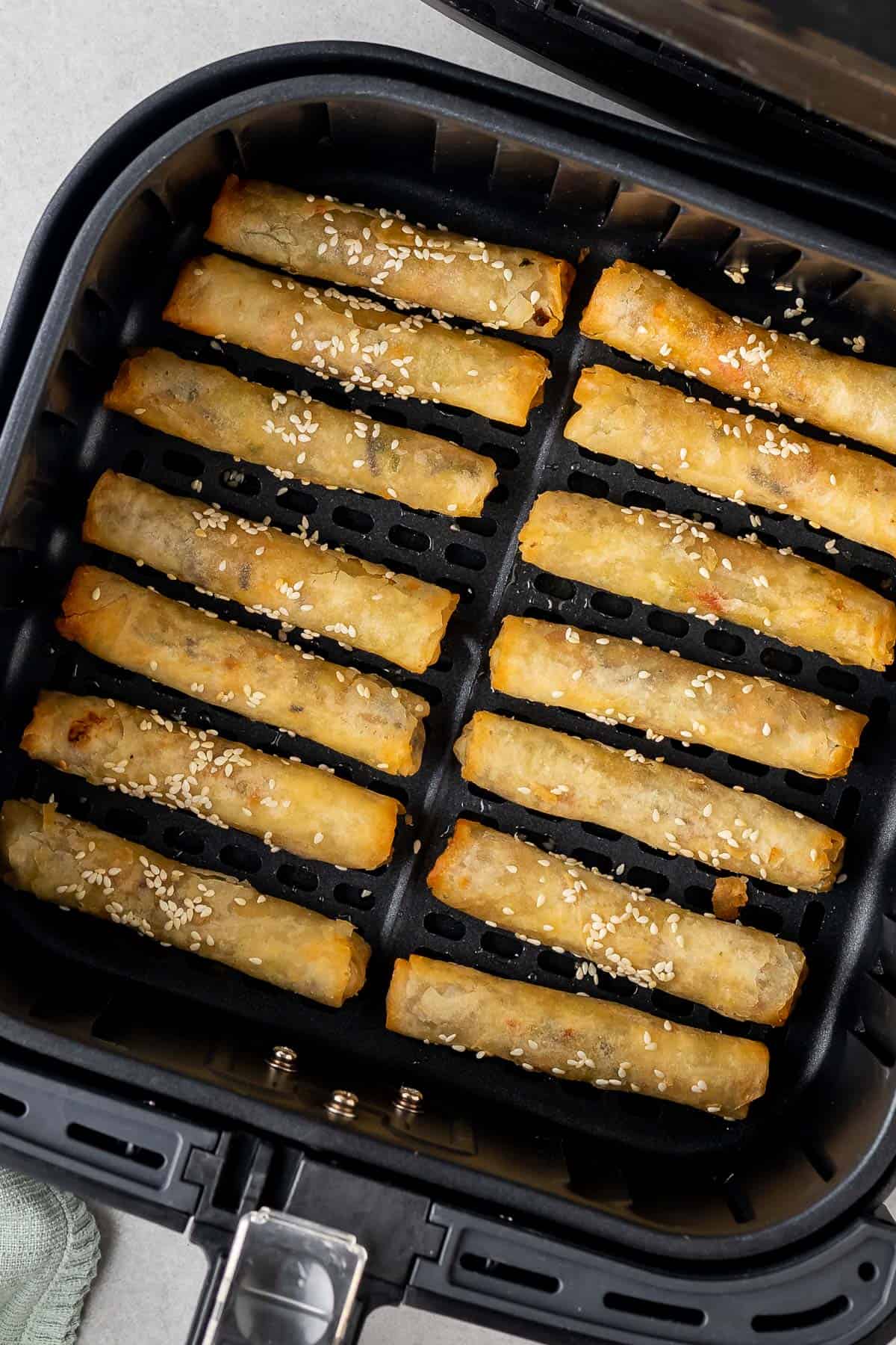 egg rolls with sesame seeds on the tops in the air fryer basket halfway through the cooking time