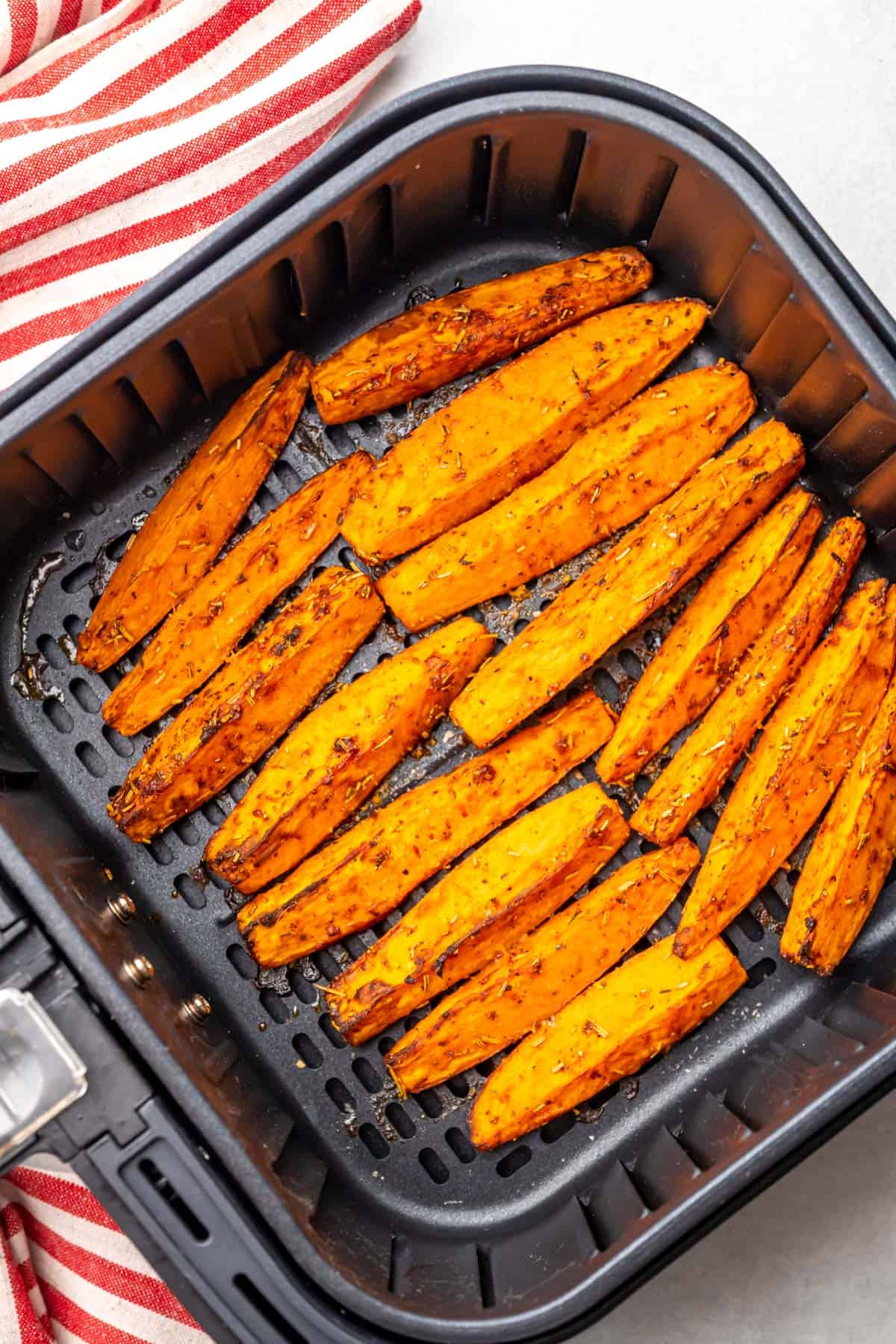 cooked and browned sweet potato wedges in the air fryer basket with a cloth