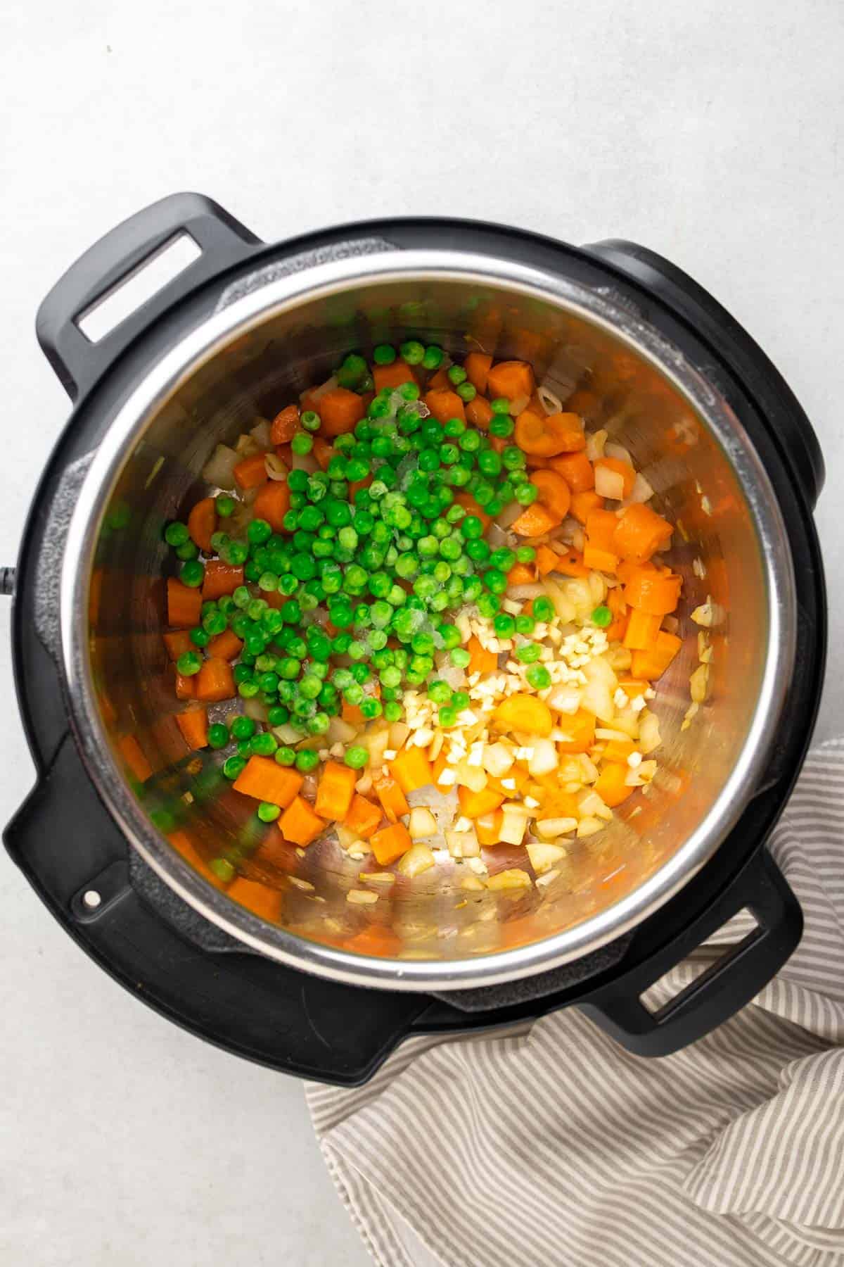 garlic and frozen peas added to the instant pot with cooked carrots and onions