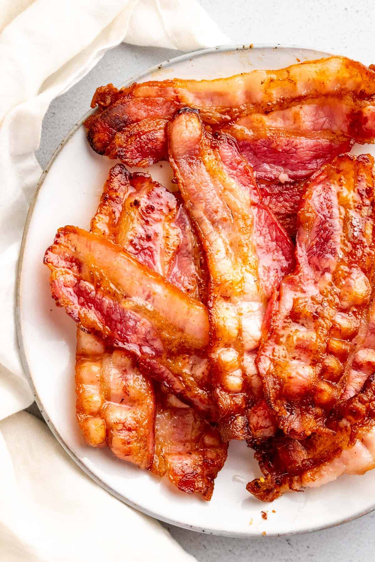 close up of crispy and perfectly cooked strips of bacon on a plate with a white decorative cloth