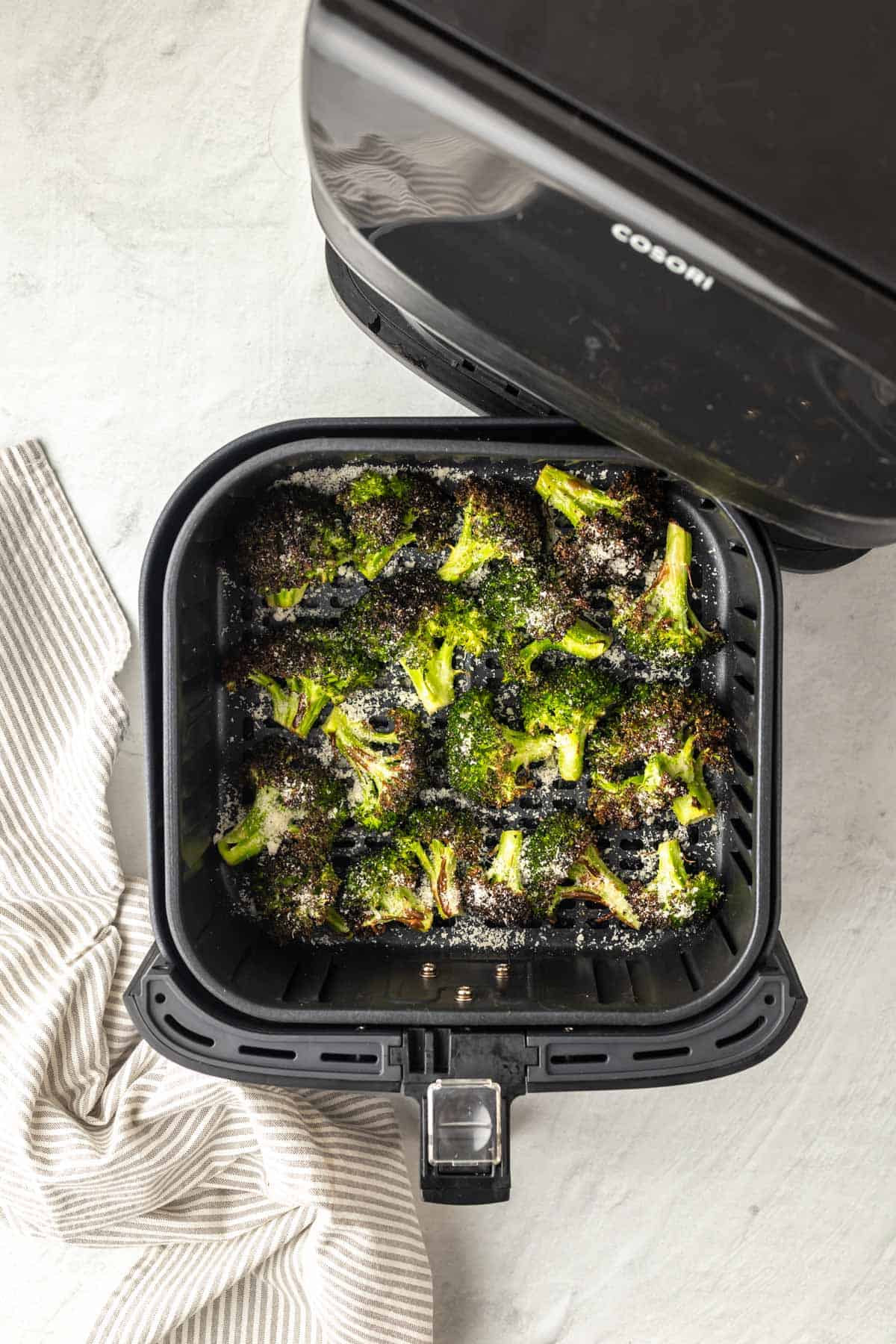 cooked broccoli in the air fryer basket with the parmesan sprinkled on top