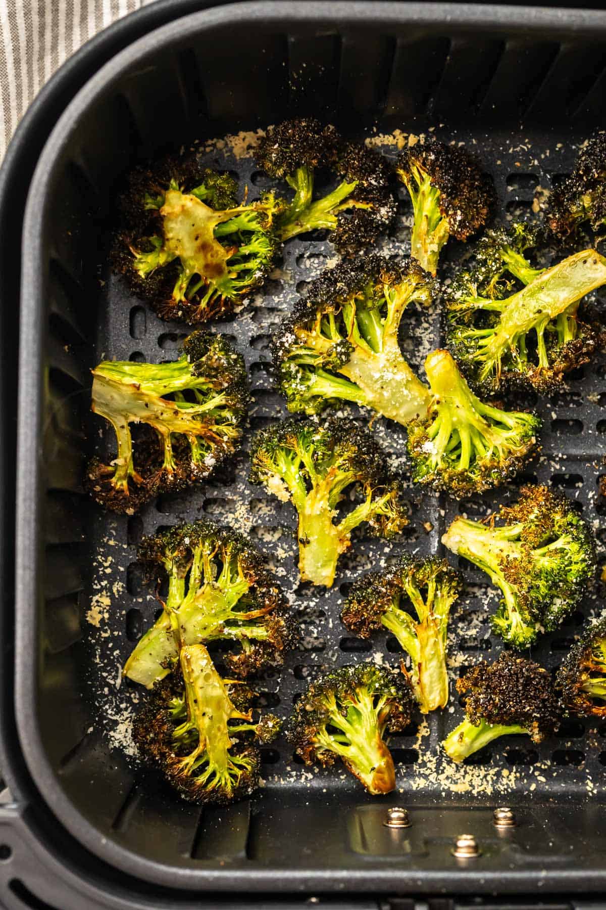 crispy broccoli florets in the air fryer basket and a striped cloth to the side