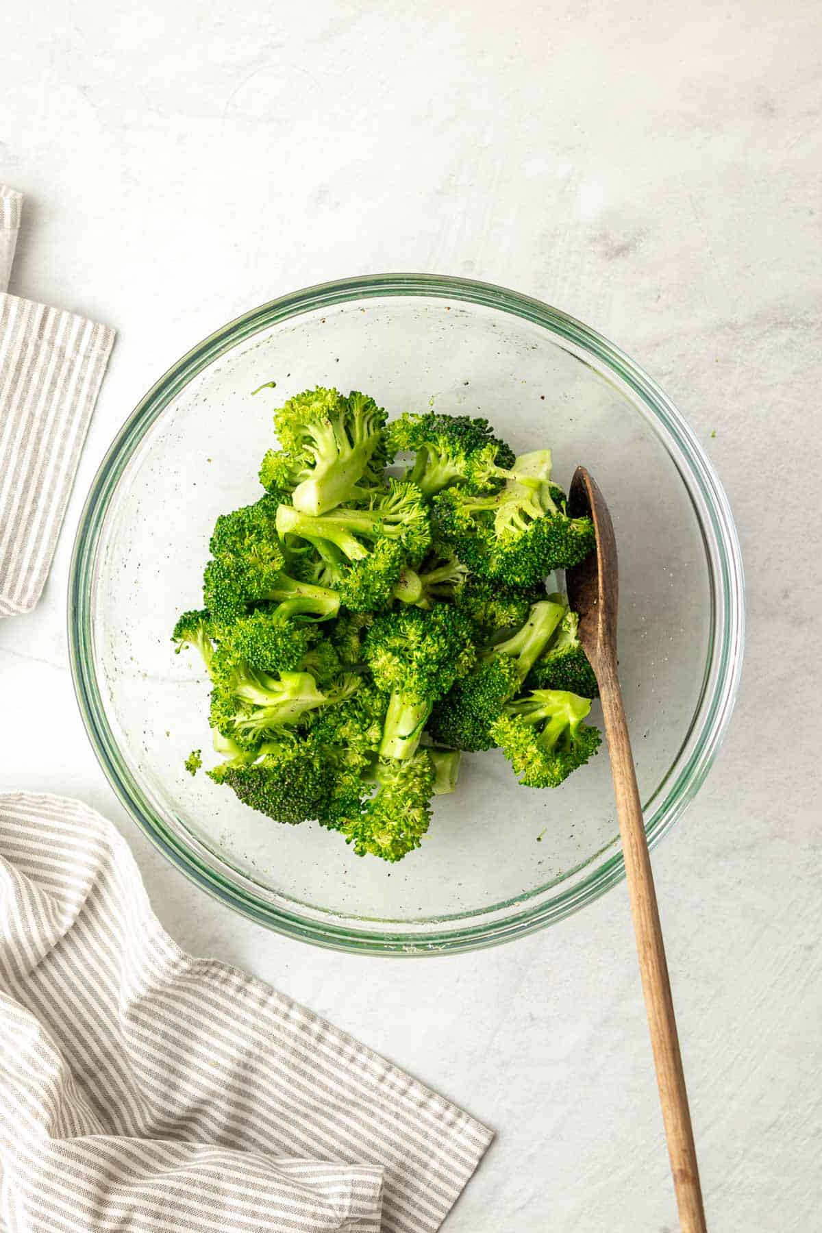 broccoli florets in a glass bowl mixed with a wooden spoon