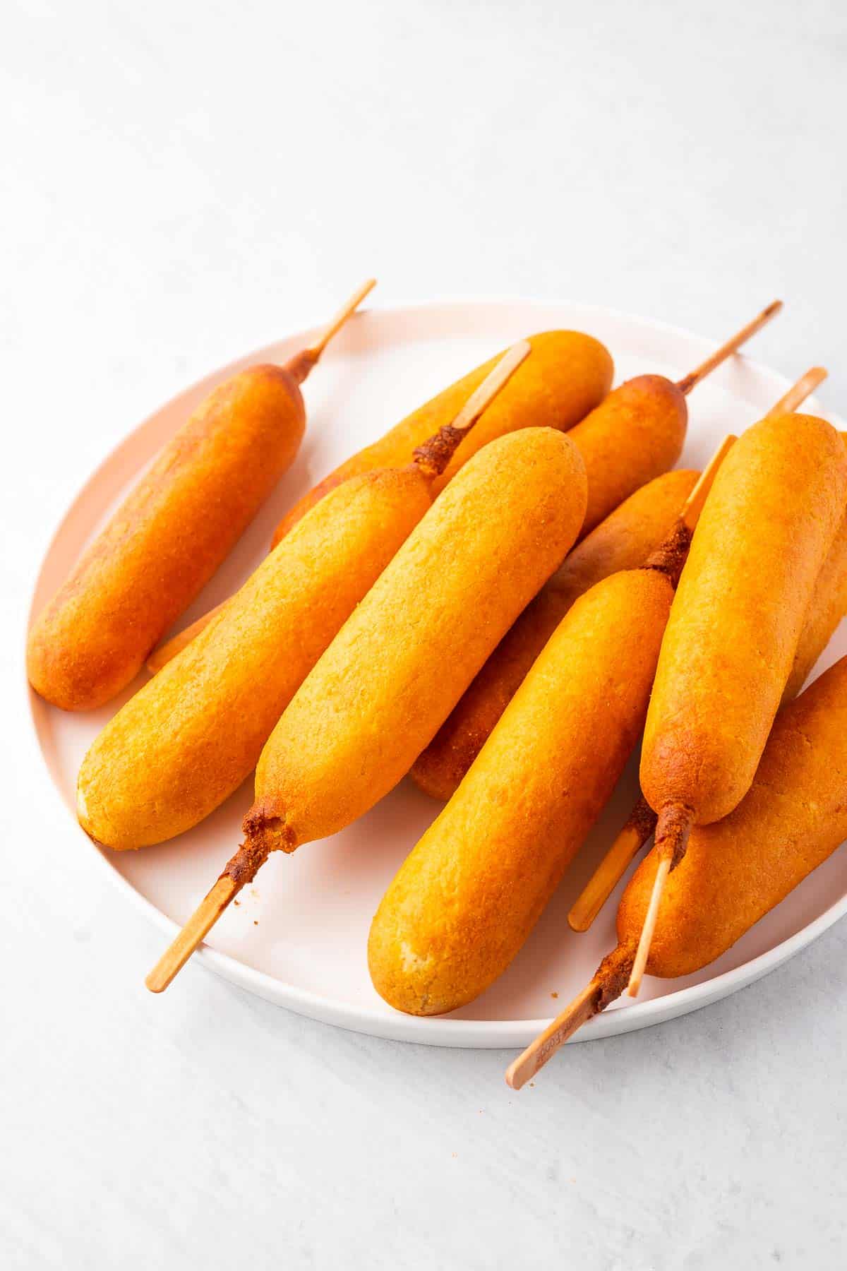 a white plate with a pile of cooked crispy corn dogs on