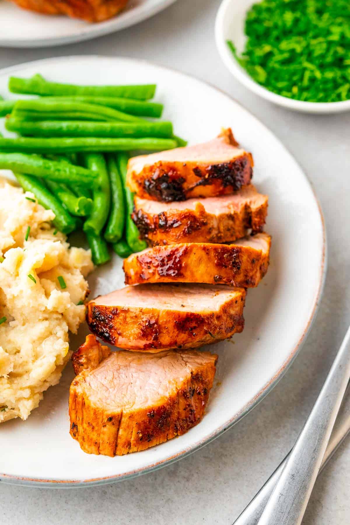 sliced pork tenderloin served with green beans and mashed potatoes