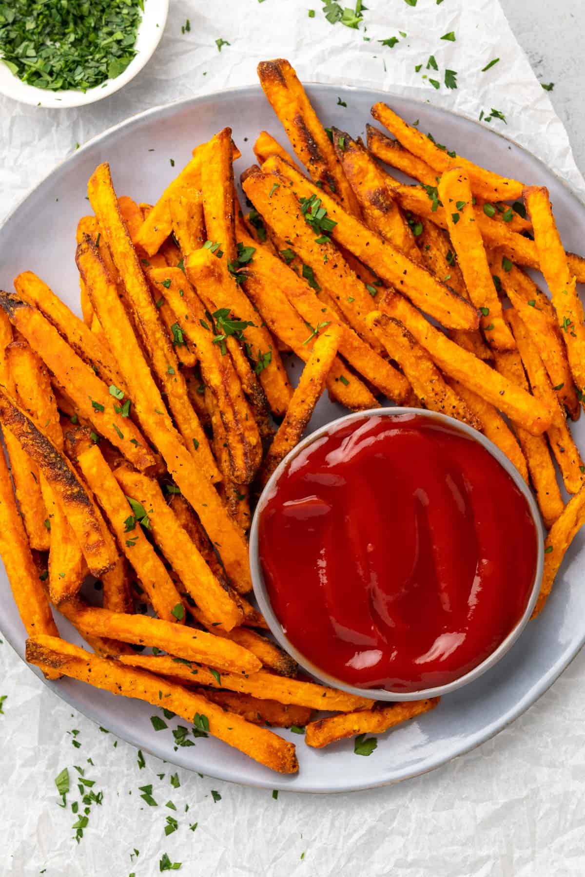 crispy sweet potato fries on a plate garnished with fresh herbs and served with ketchup