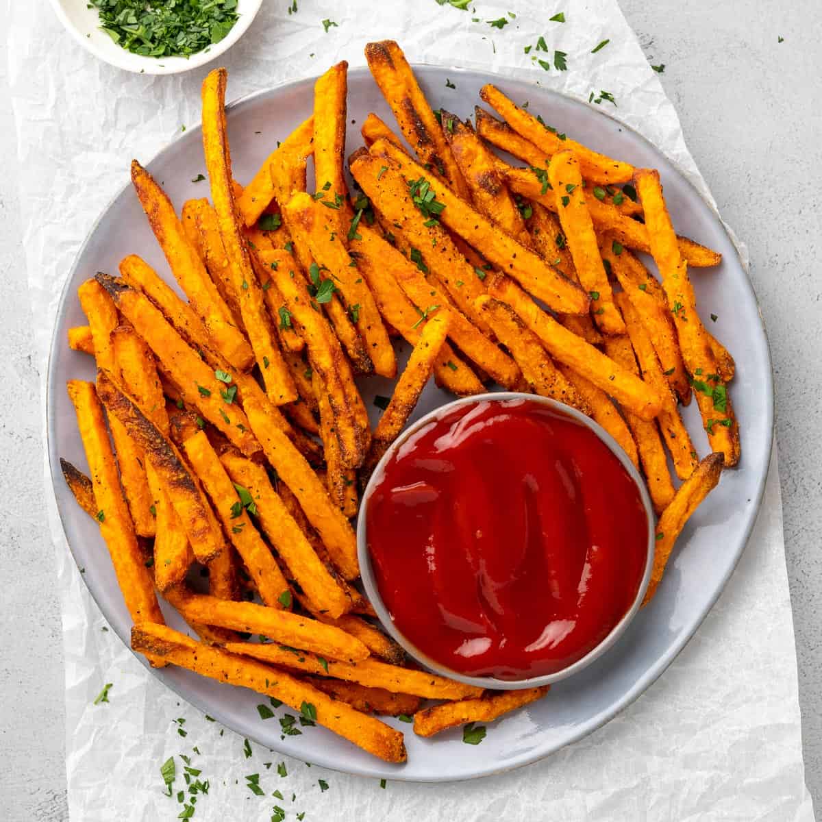air fried sweet potato fries on a plate, garnished with fresh herbs, served with ketchup
