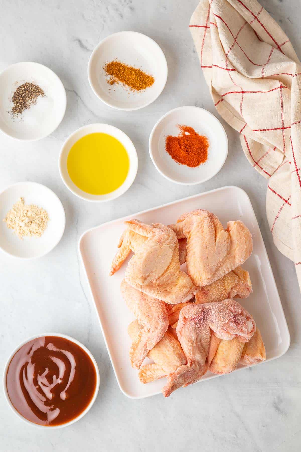 ingredients for the air fryer chicken wings laid out in white dishes with a red and white patterned cloth to one side