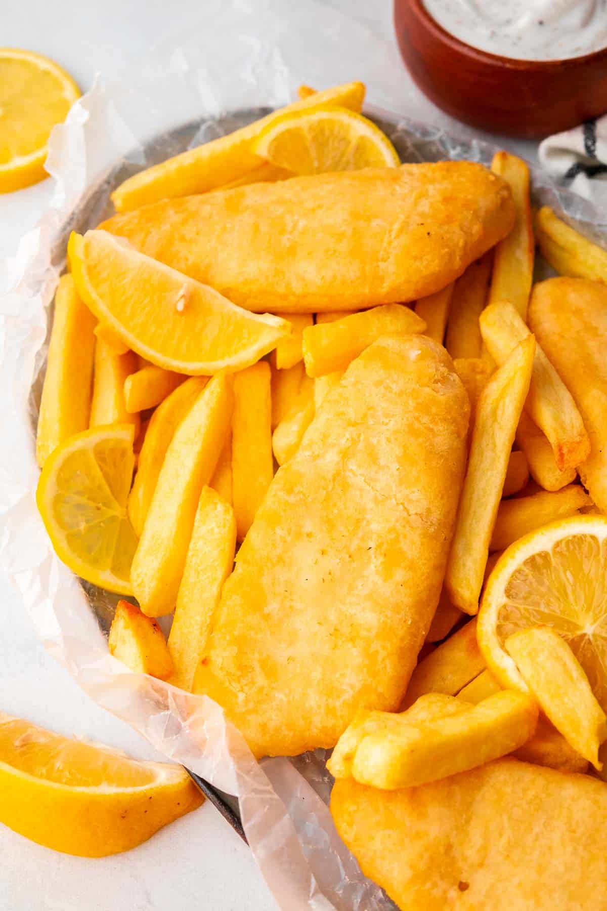 golden and crispy fish fillets on a plate of fries served with lemon wedges