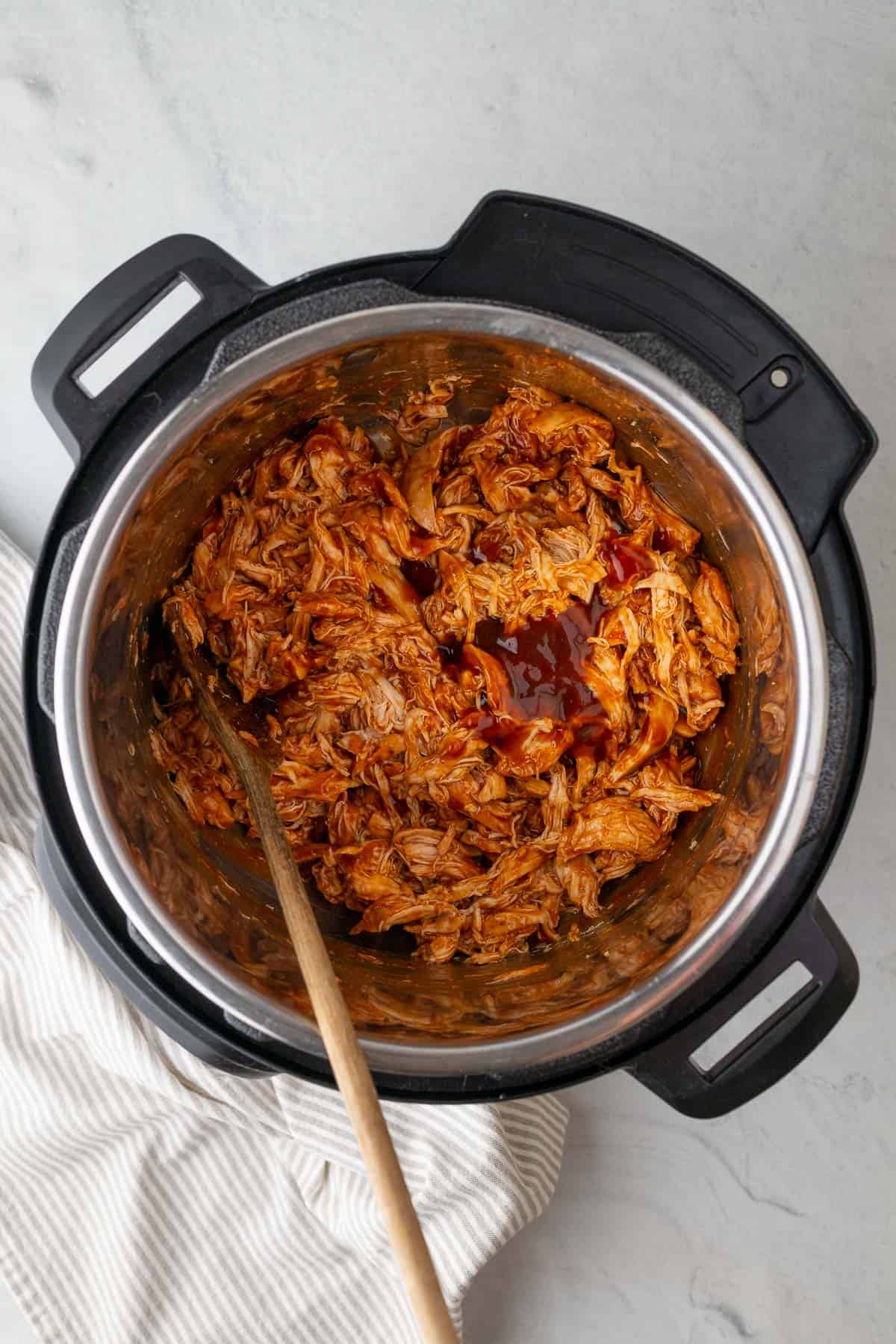 barbecue pulled chicken in the instant pot with a wooden spoon