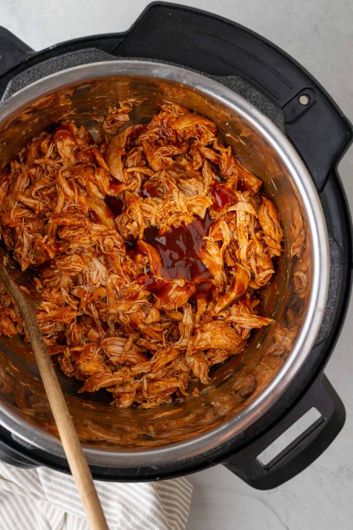 close up of the barbecue shredded chicken in the instant pot with a wooden spoon