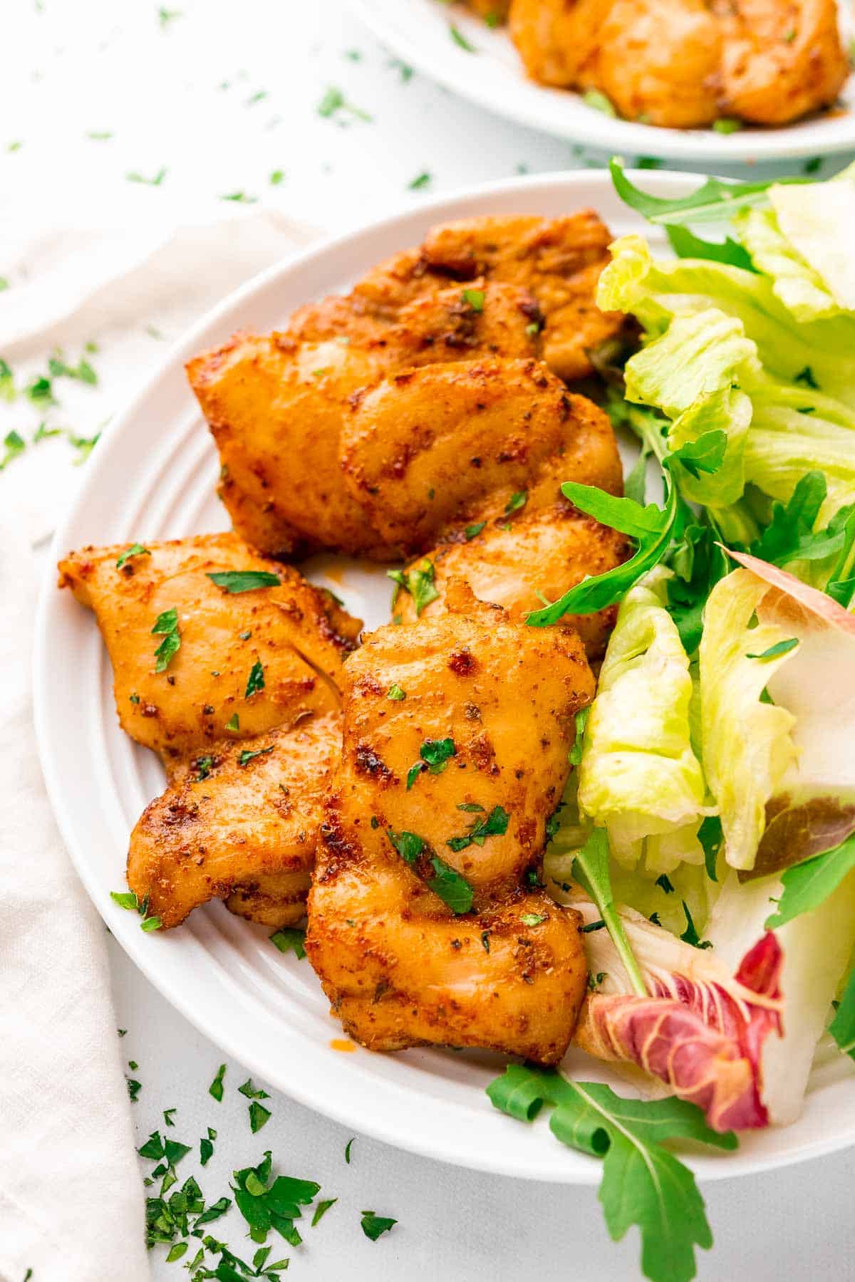 a pile of chicken thighs on a plate served with a green salad and freshly chopped herbs