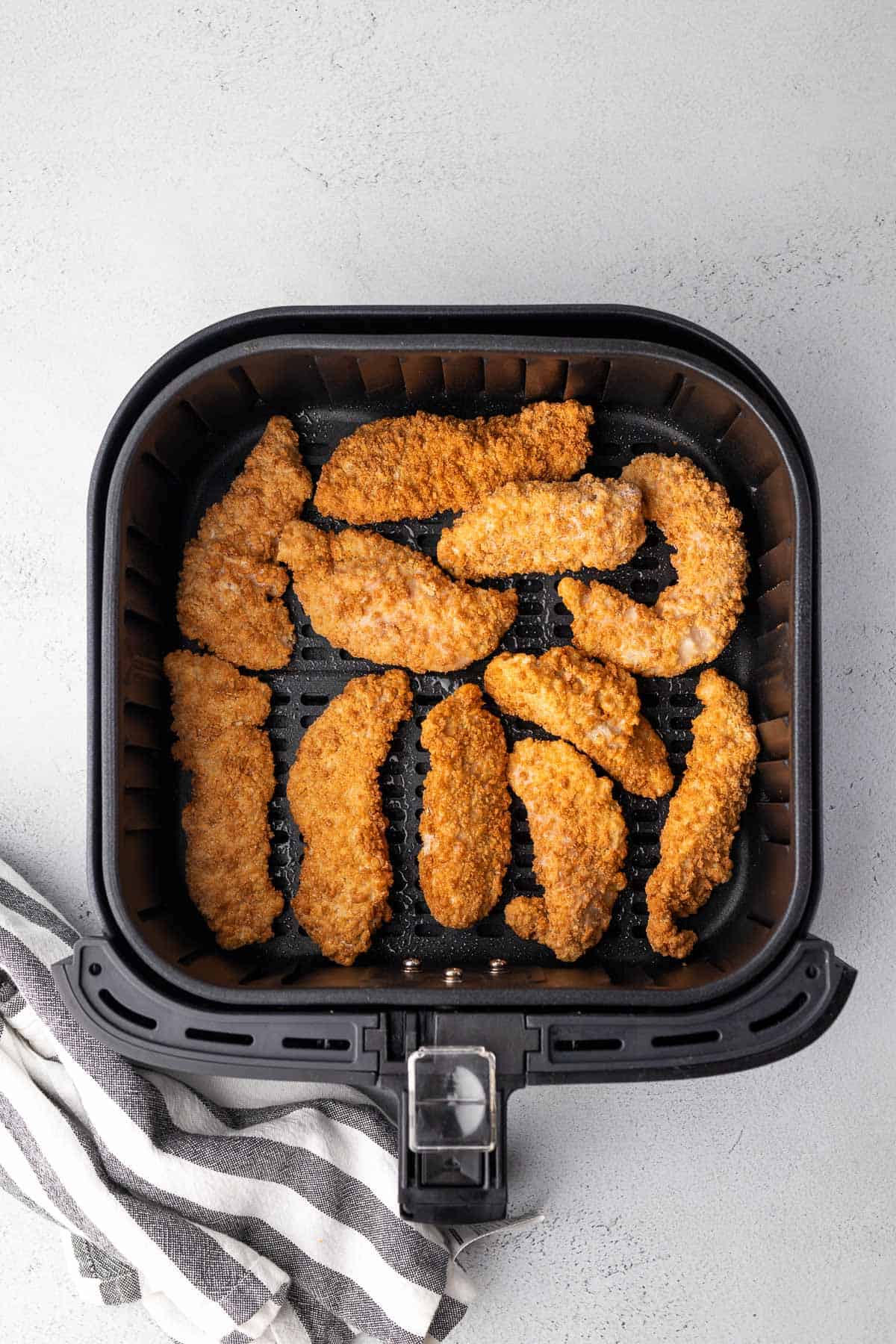 frozen chicken tenders in the air fryer basket before cooking with striped cloth to one side