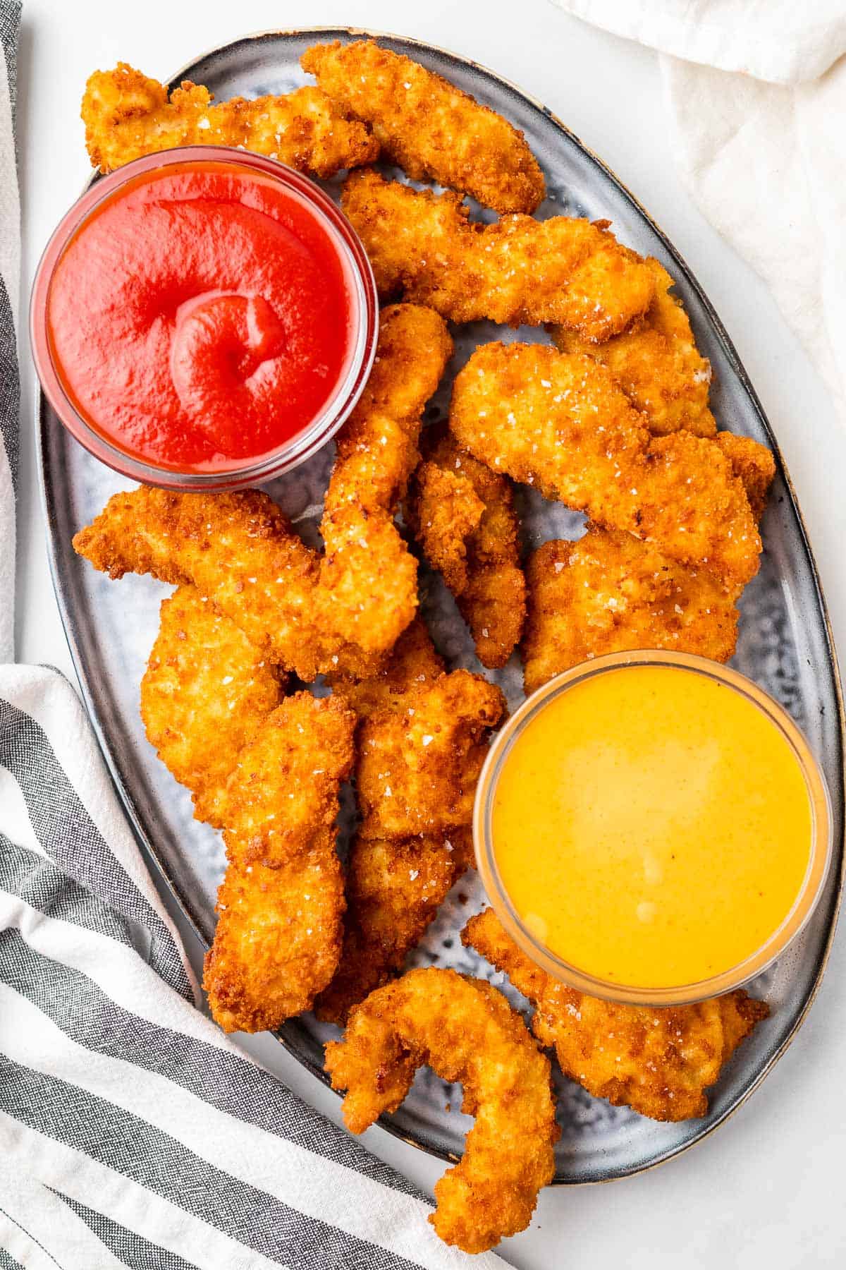 close up of the crispy chicken tenders with a mustard sauce and ketchup on a platter