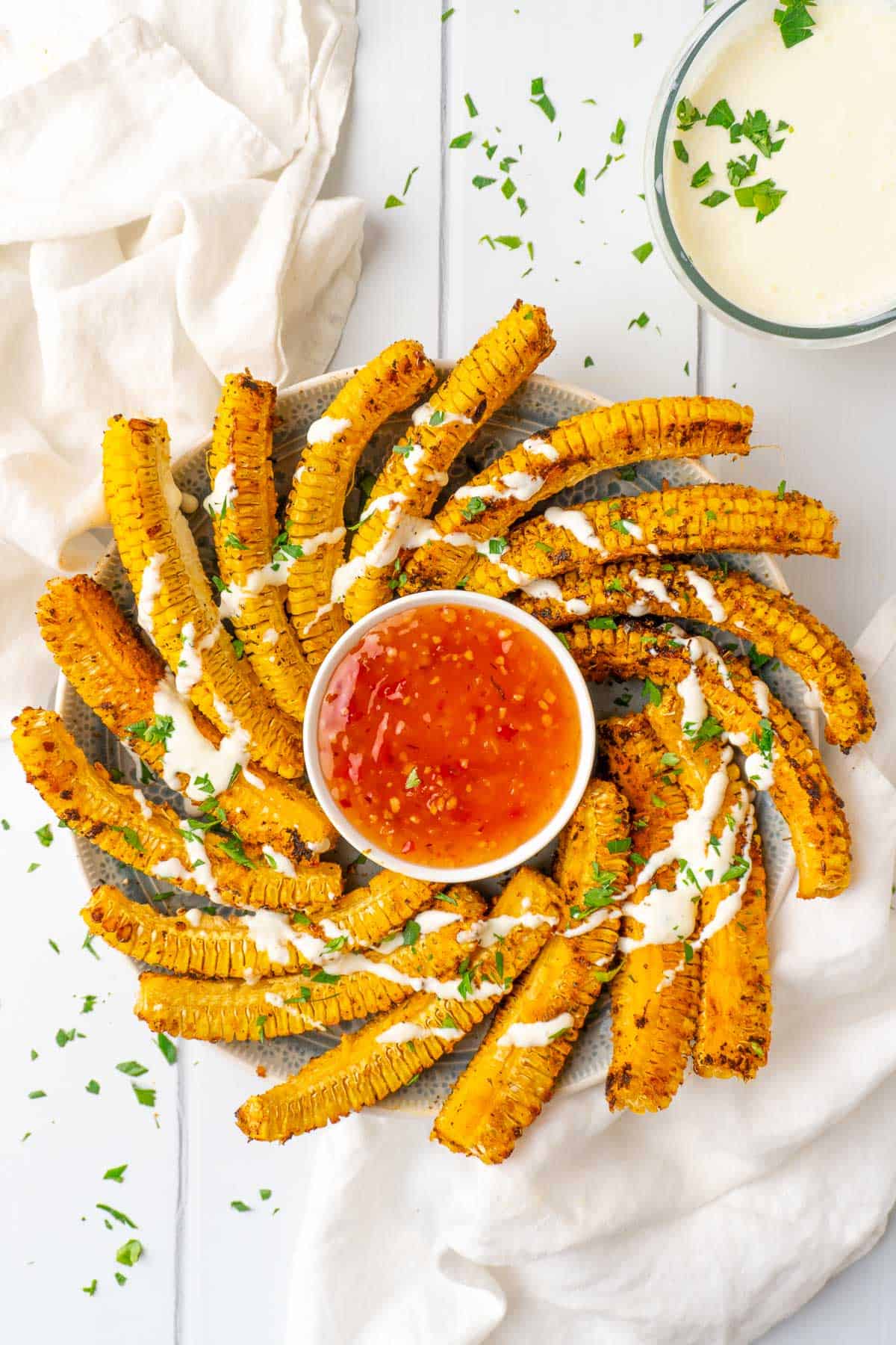 cooked corn ribs arranged on a platter in a circle garnished with a creamy sauce and fresh herbs
