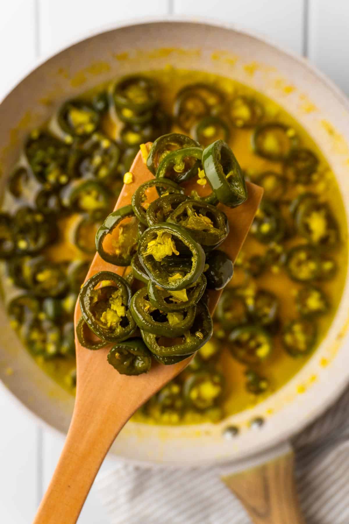 close up of removing the spiced jalapeños from the syrup with a slotted wooden spoon