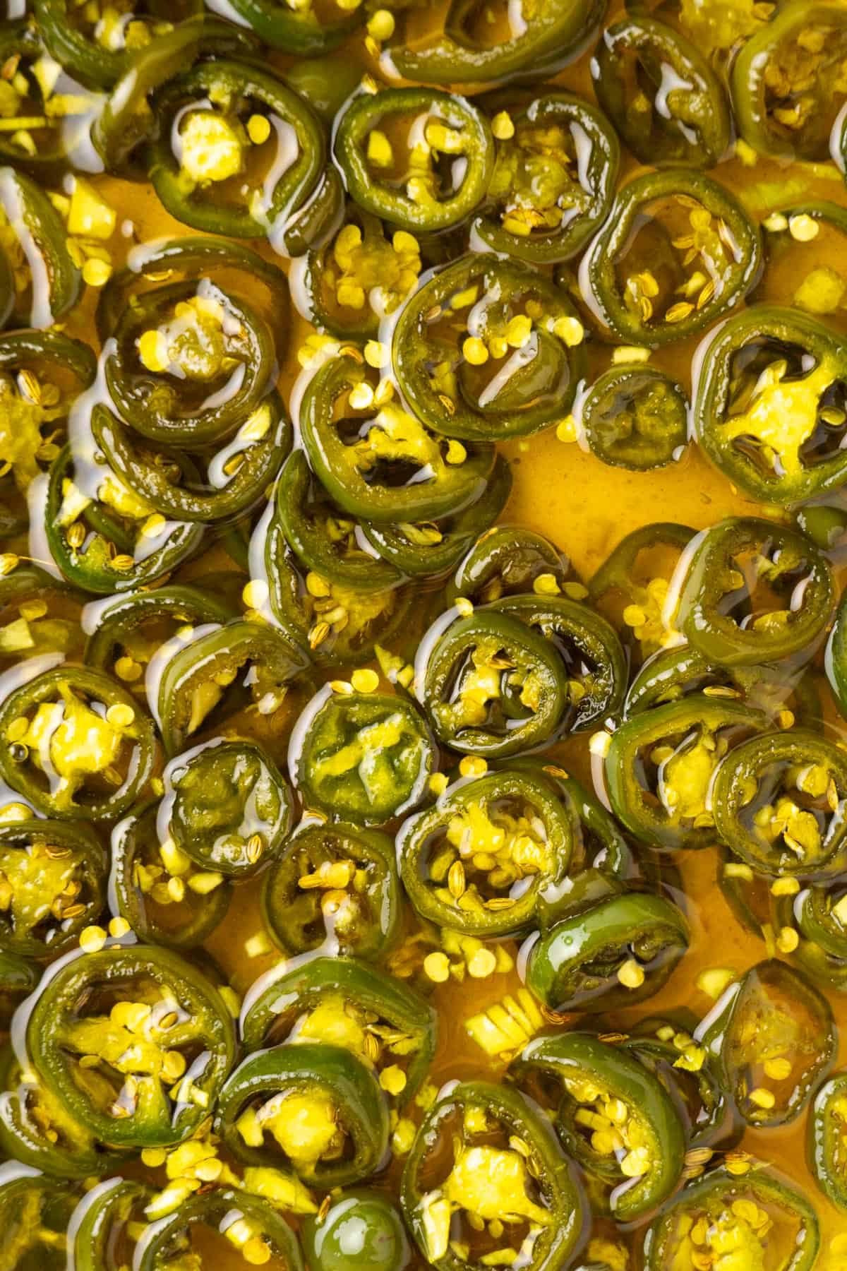 close up of the sliced jalapeños cooking in the vinegar syrup in a pan