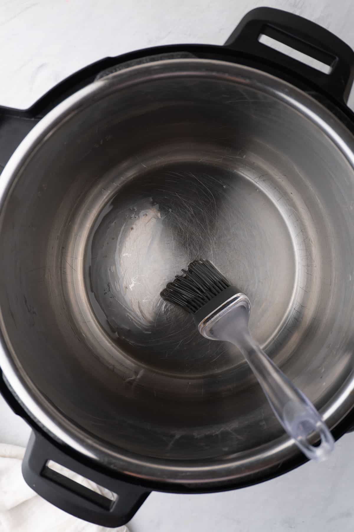 a silicon brush brushing oil over the bottom of the Instant Pot before adding the other ingredients