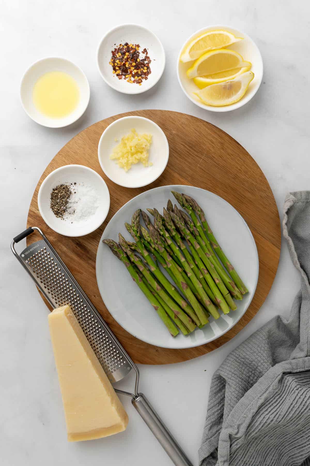 ingredients for the asparagus laid out in white bowls on a wooden board with a grey decorative cloth to the right side