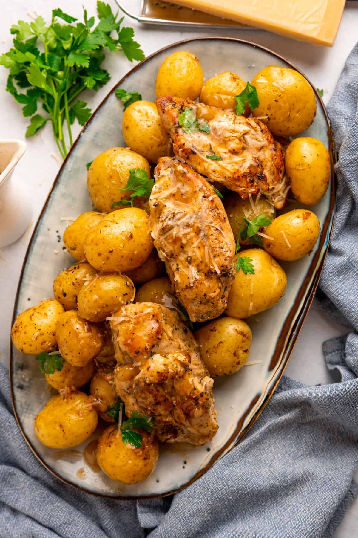 a platter full of chicken and potatoes garnished with parsley and fresh parmesan 