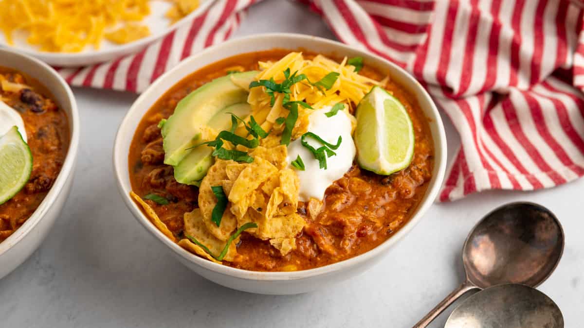 a bowl of chili served and garnished with corn chips, avocado slices, sour cream and cilantro 