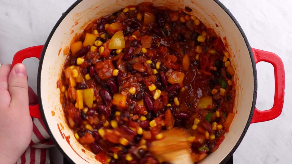 mixing the kidney beans and corn into the spices and herbs in the red pot 