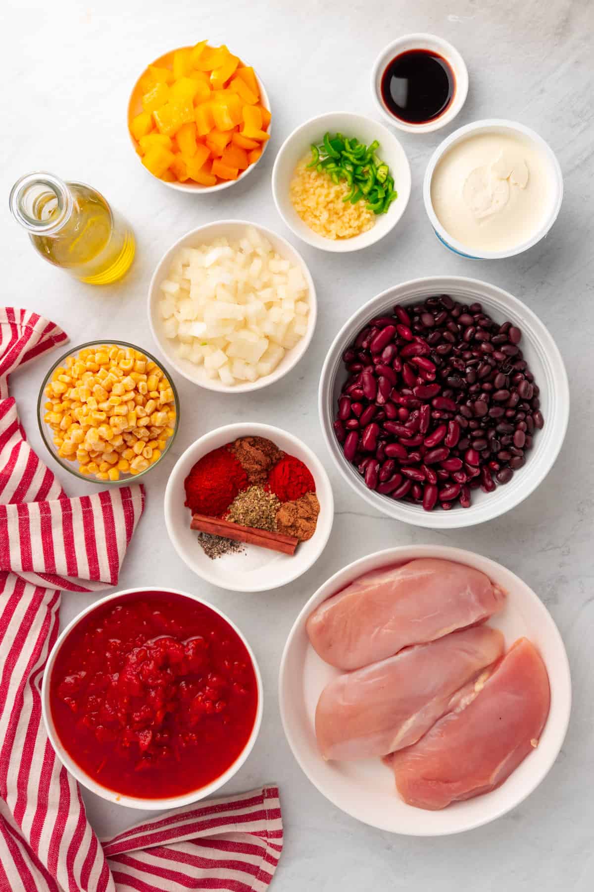 ingredients for the chicken chili laid out in white bowls and dishes with a red striped cloth to the left side 