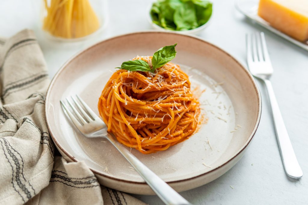 A plated dish of rotini pasta thoroughly coated in a white, creamy cottage cheese sauce, garnished with fresh green herbs.