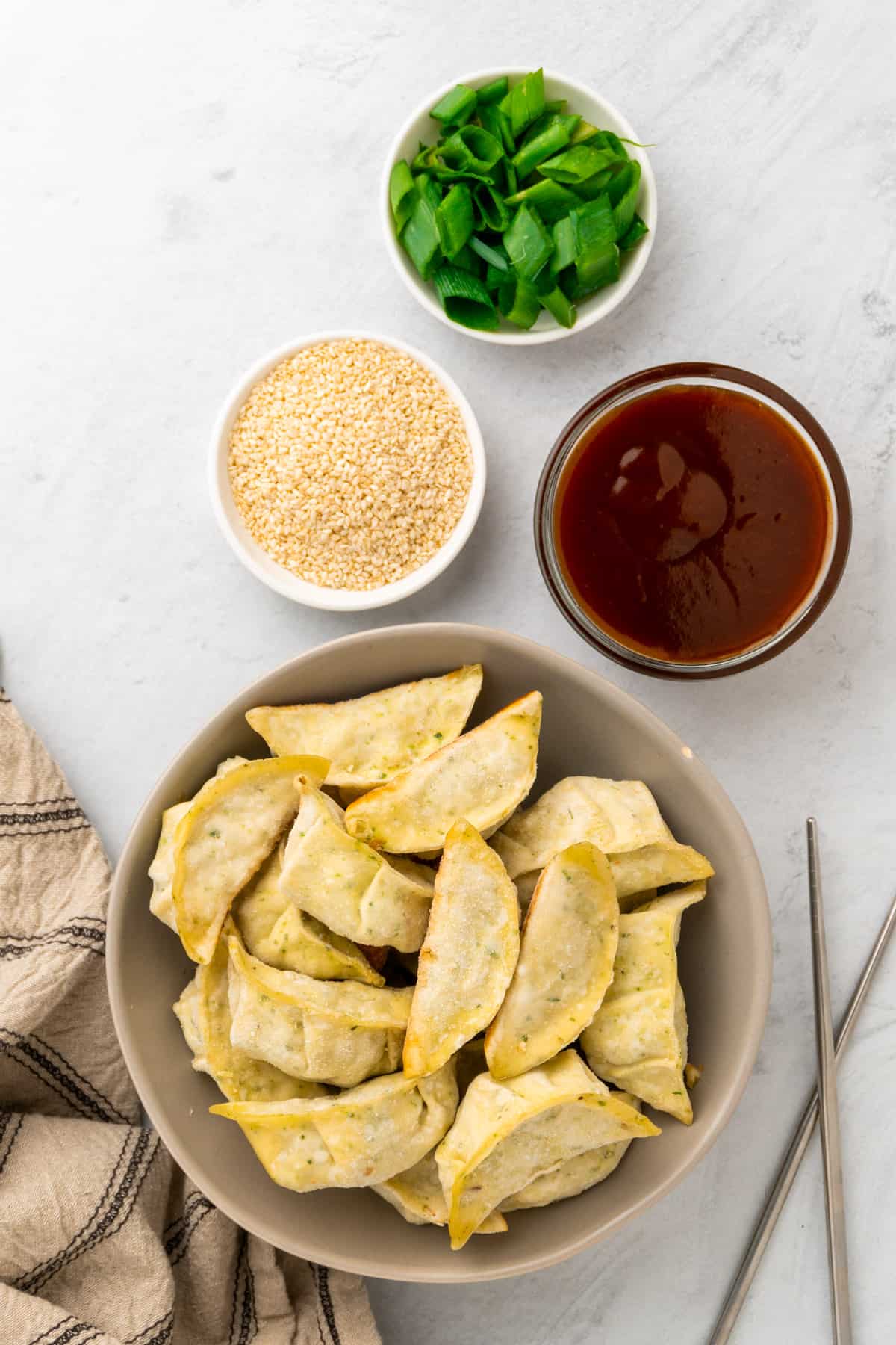 frozen mini wontons, sauce, green onions and sesame seeds on table