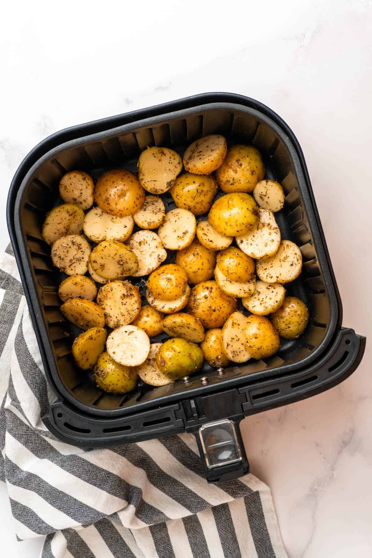 Seasoned Greek potatoes in a single layer in the air fryer basket. 
