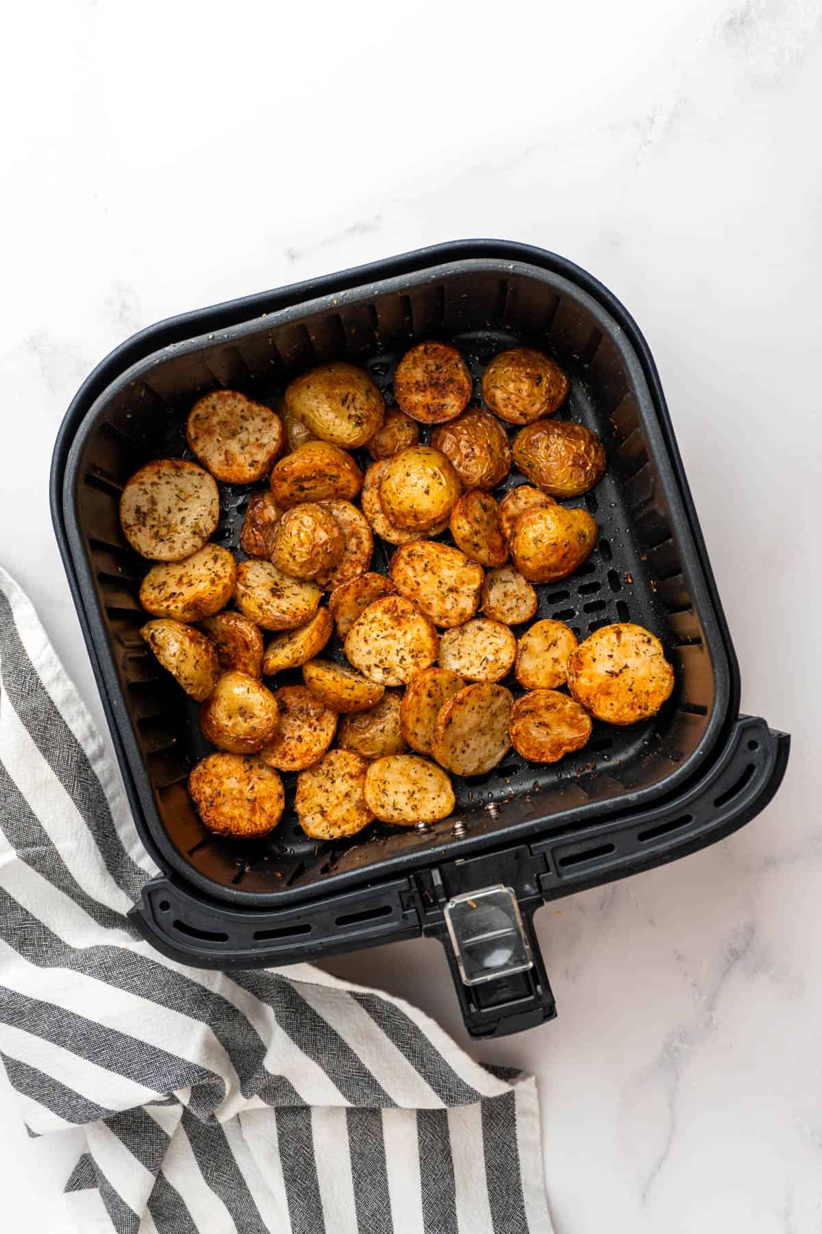 Crispy and golden air fryer greek potatoes in the air fryer basket after cooking. 