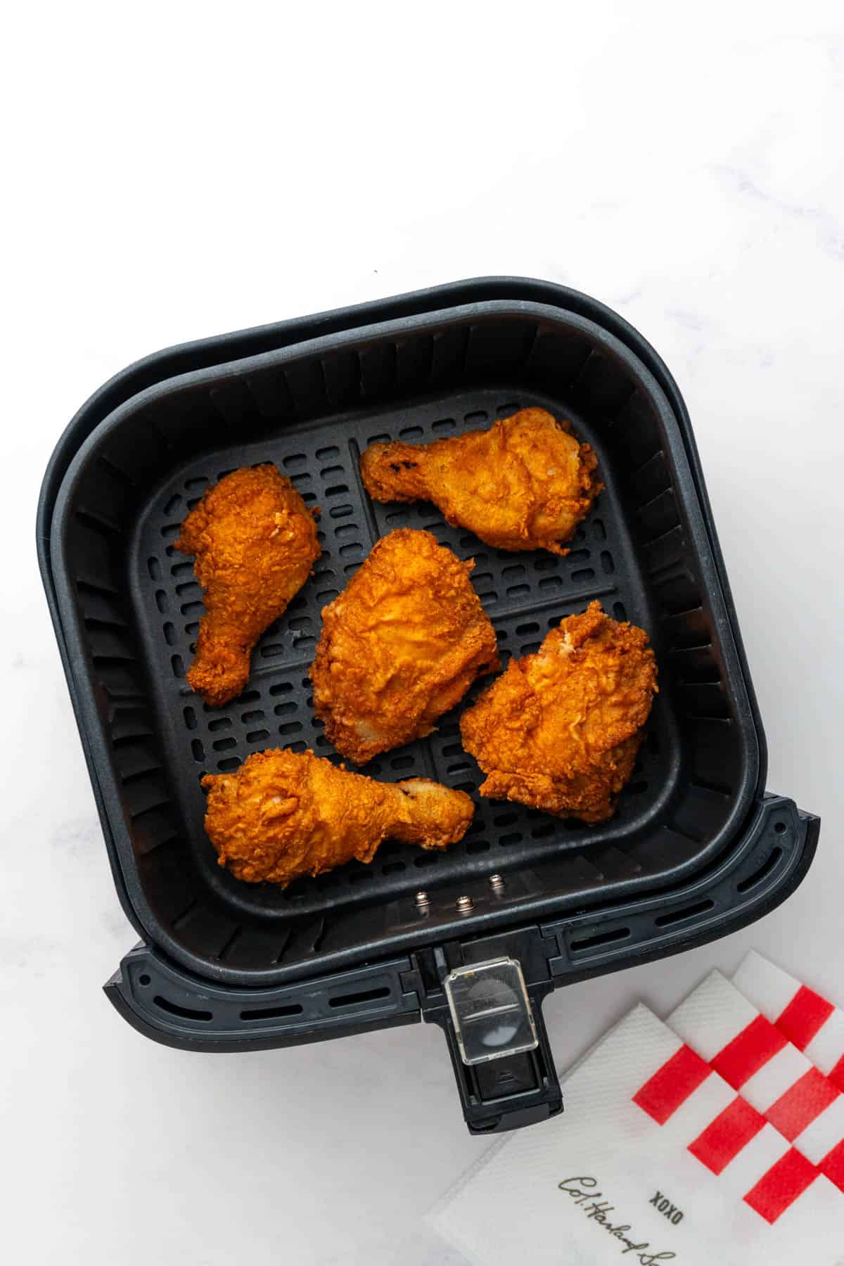 Five pieces of fried chicken laid out in the air fryer basket with some napkins for decoration. 