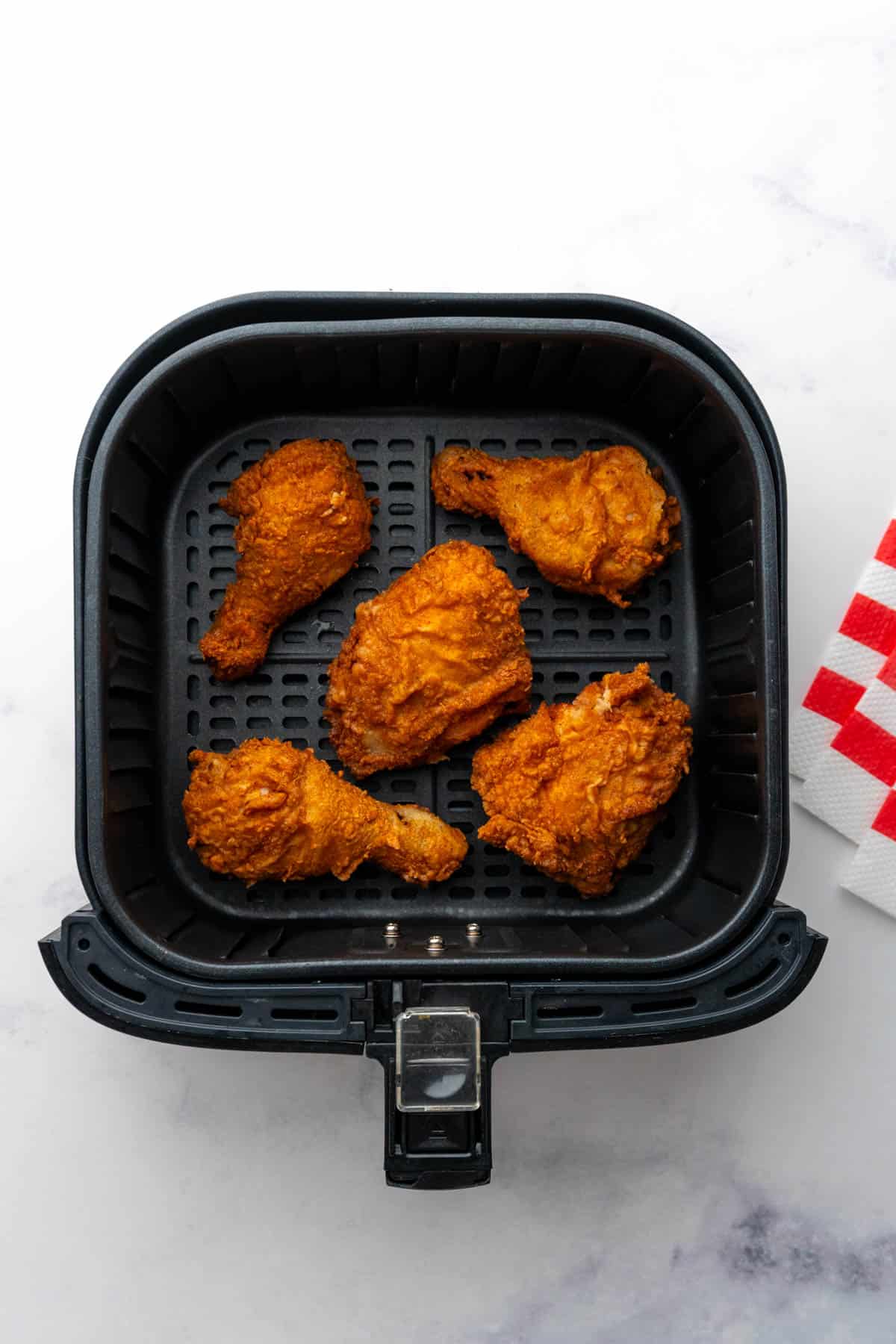Reheated pieces of fried chicken in the air fryer basket after being reheated till crispy. 