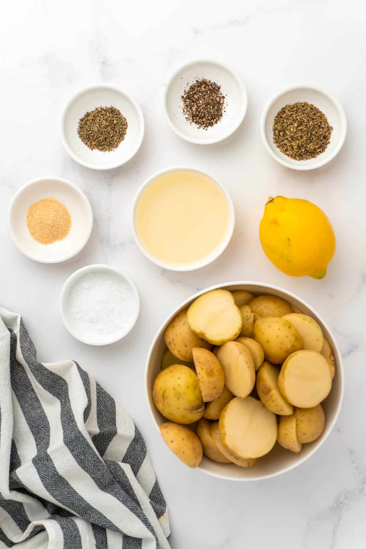 Ingredients for the air fryer Greek potatoes laid out in small ceramic dishes on a white background. 