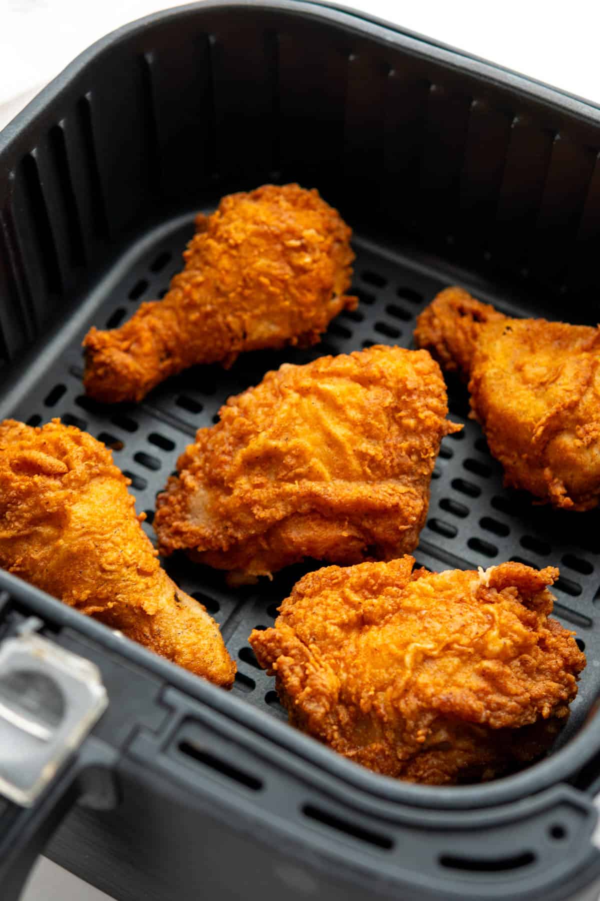 Pieces of fried chicken in a single layer in the air fryer basket. 