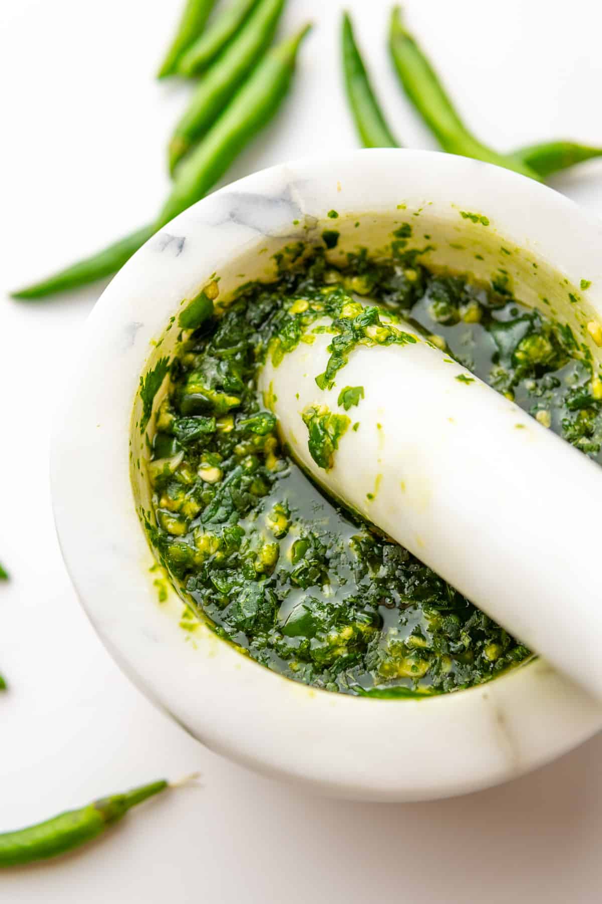 Spicy green chili sauce in a mortar and pestle with fresh chillies around the mortar.