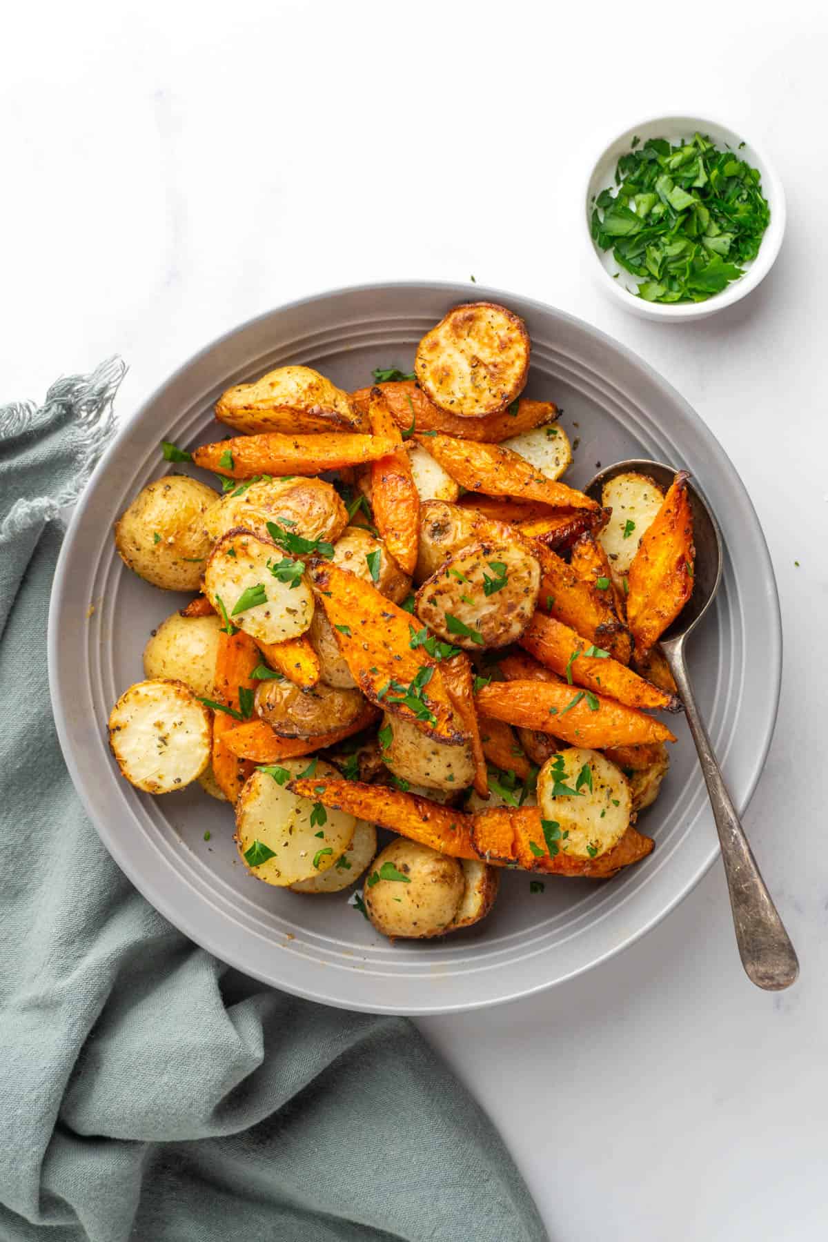 Air fryer roasted carrots and potatoes served with green parsley and a spoon in a grey bowl. 