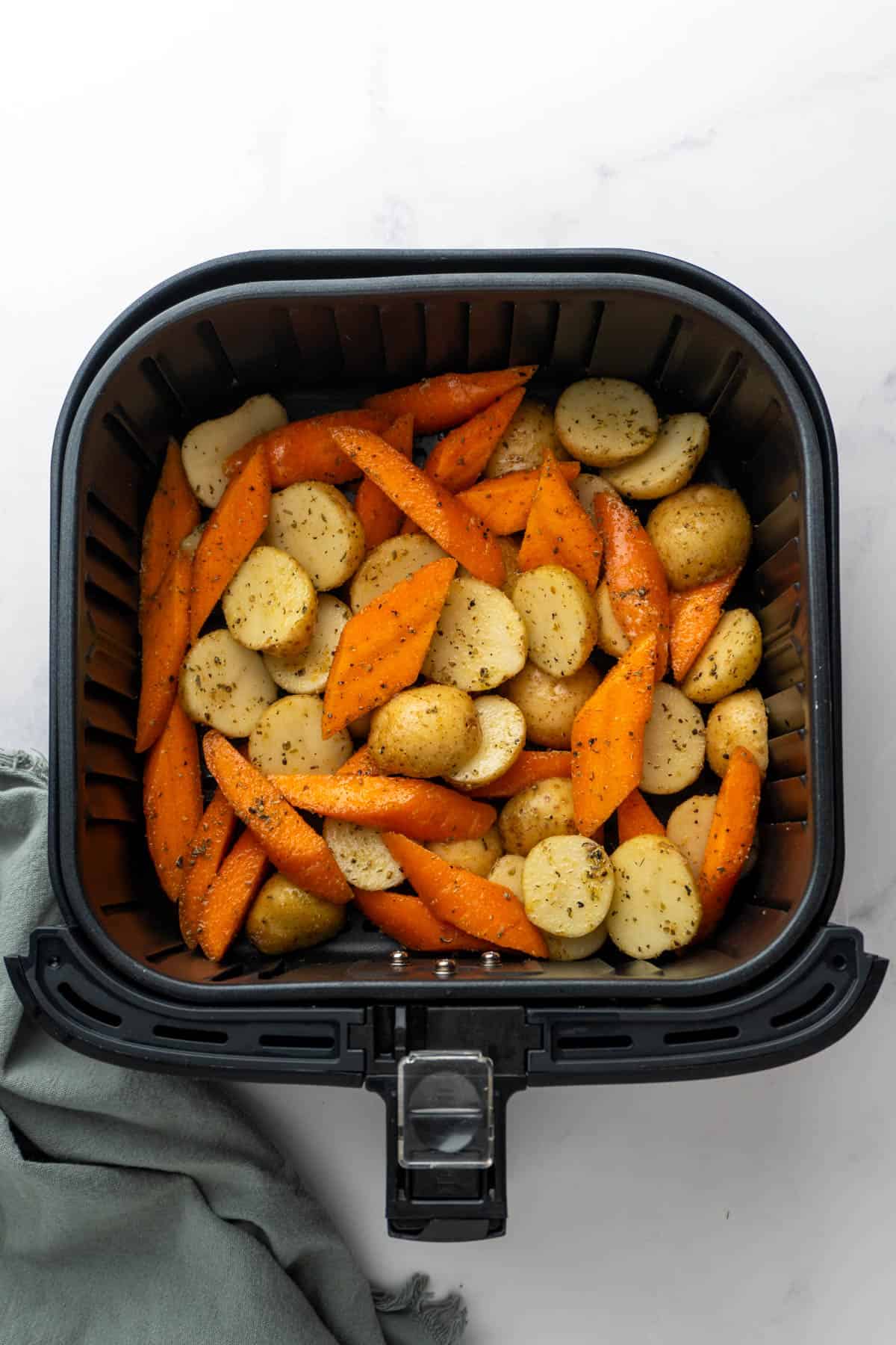 The seasoned carrots and potatoes laid out in a single layer in the air fryer basket. 