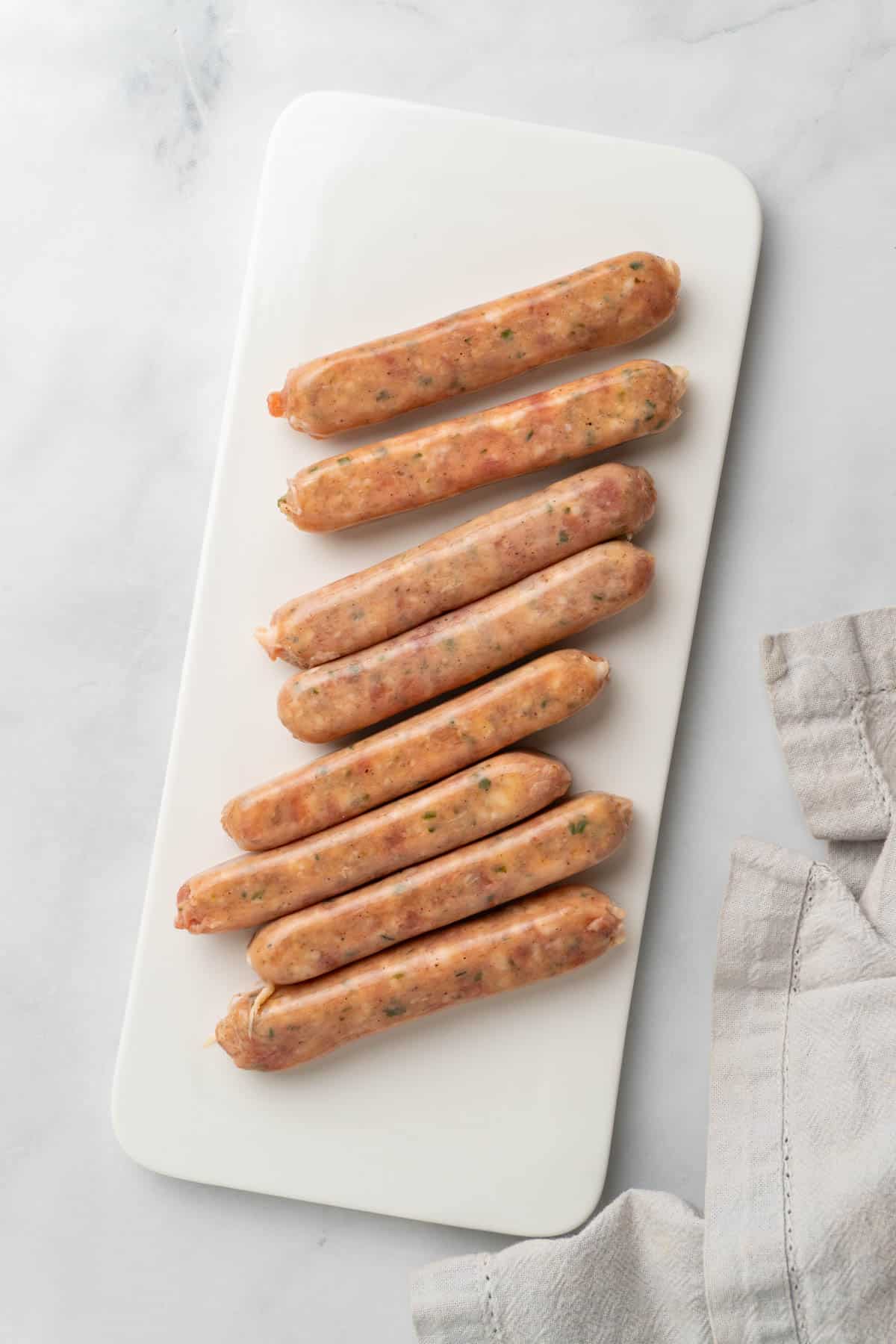 Raw chicken sausages laid out on a white serving dish, on a white background. 