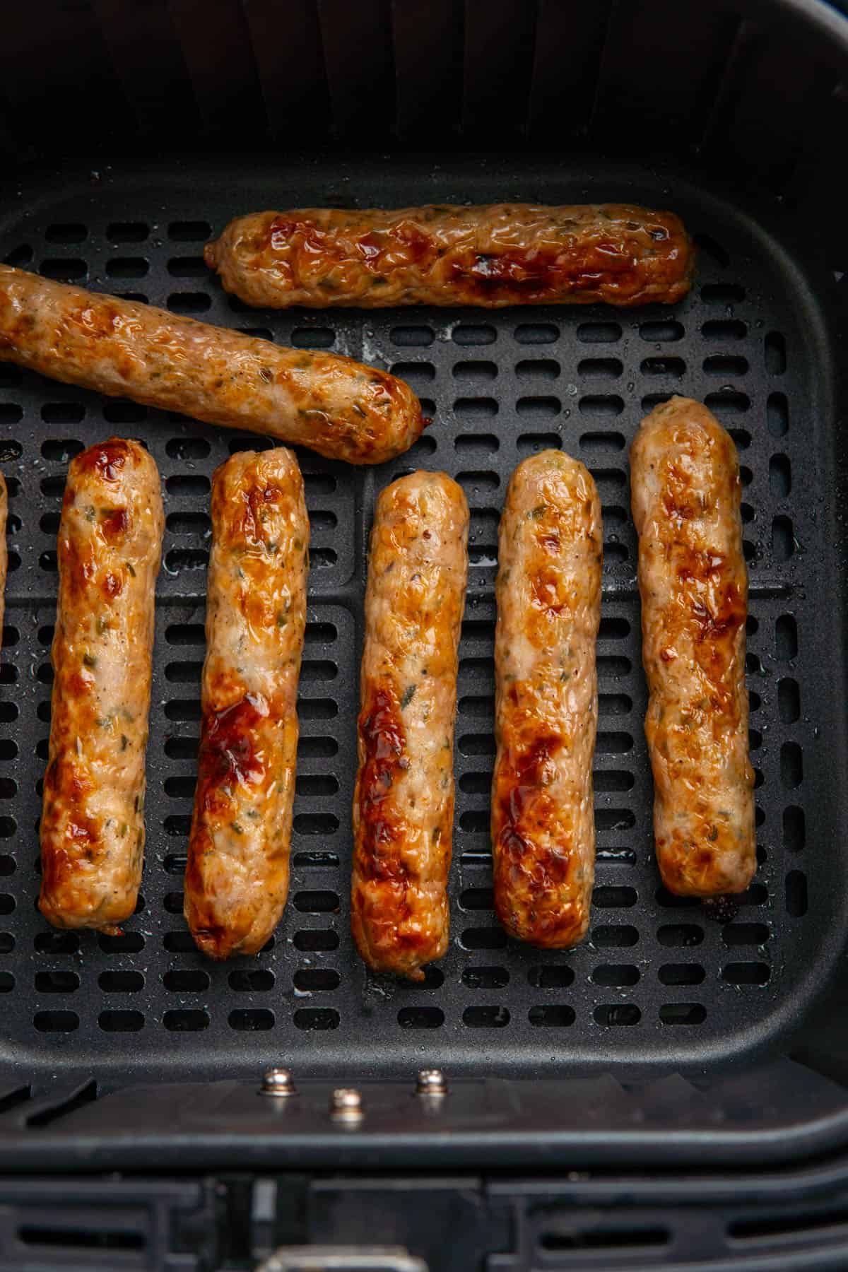 Crispy cooked chicken sausages in the air fryer basket laid out in rows. 