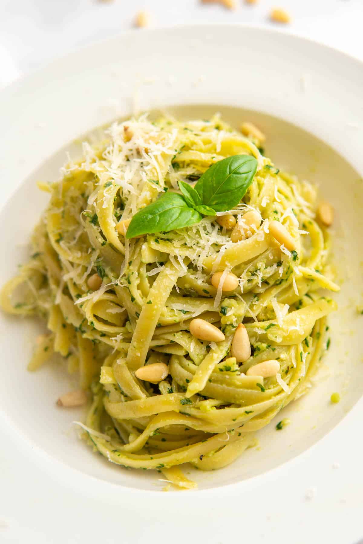 Basil pesto pasta served in a white pasta bowl garnished with pine nuts, parmesan cheese, and fresh basil leaves.