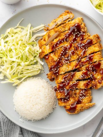 Sliced chicken katsu served on a plate with sliced cabbage and cooked rice.