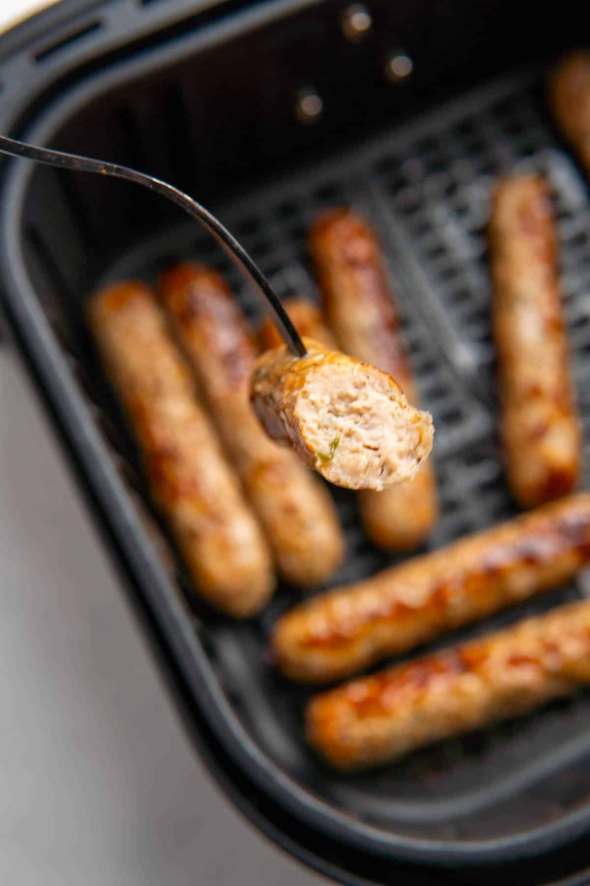 A fork showing the inside of a chicken sausage, the other sausages are blurred in the background. 