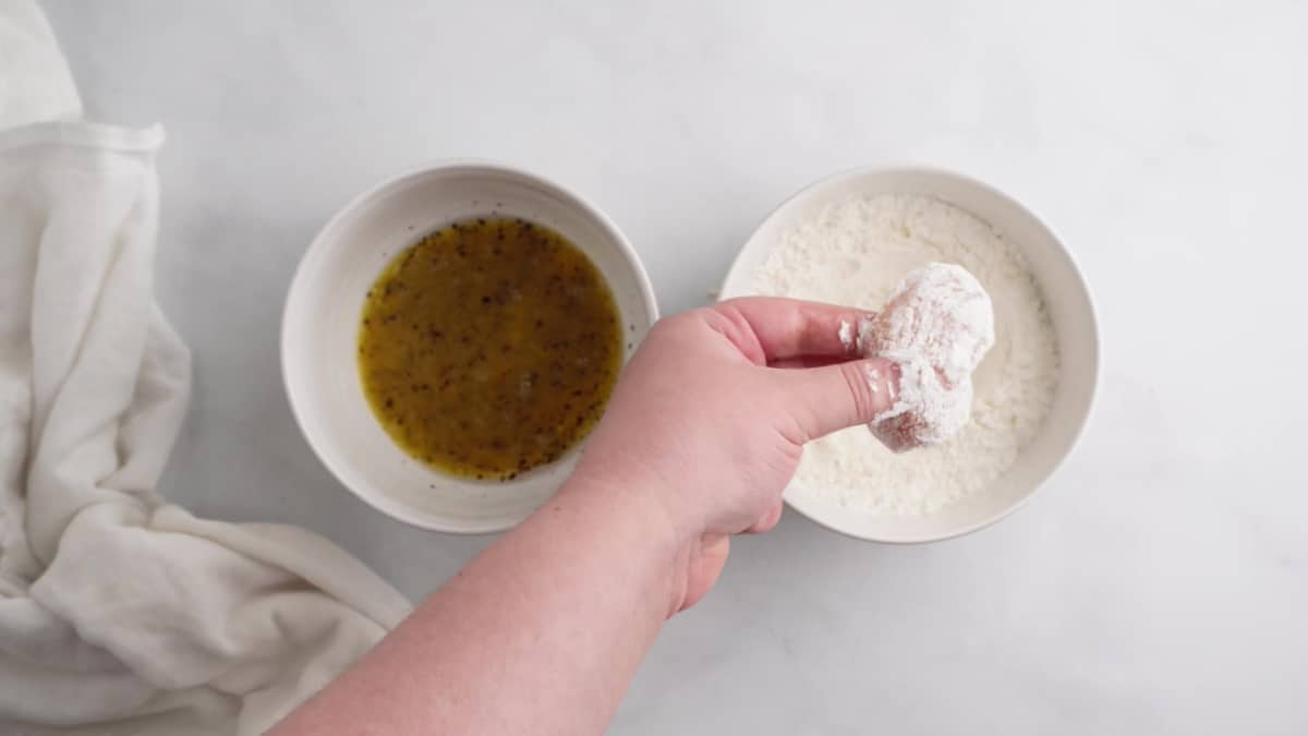 Dipping a piece of chicken into the dry ingredients mixture. 